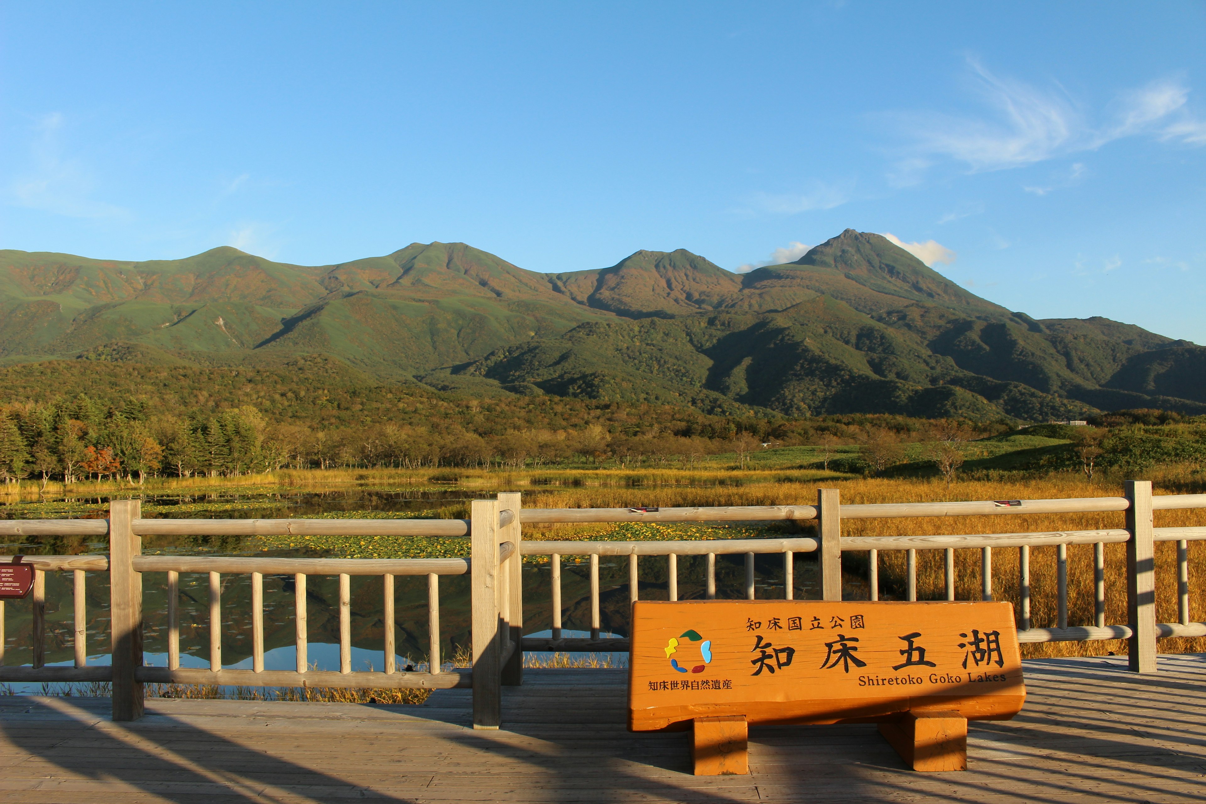 Wooden bench and sign overlooking serene mountains and calm waters