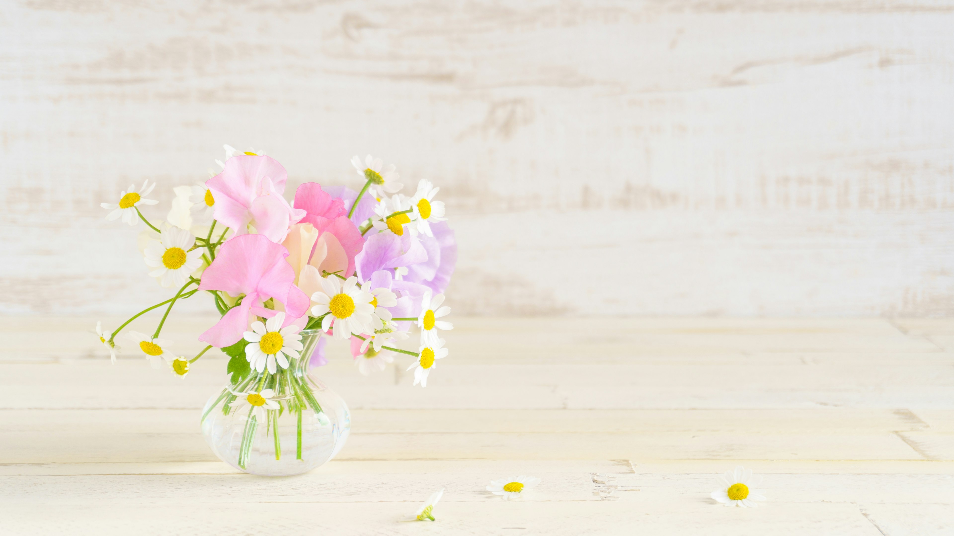 A delicate bouquet of pastel flowers in a glass vase on a light wooden background