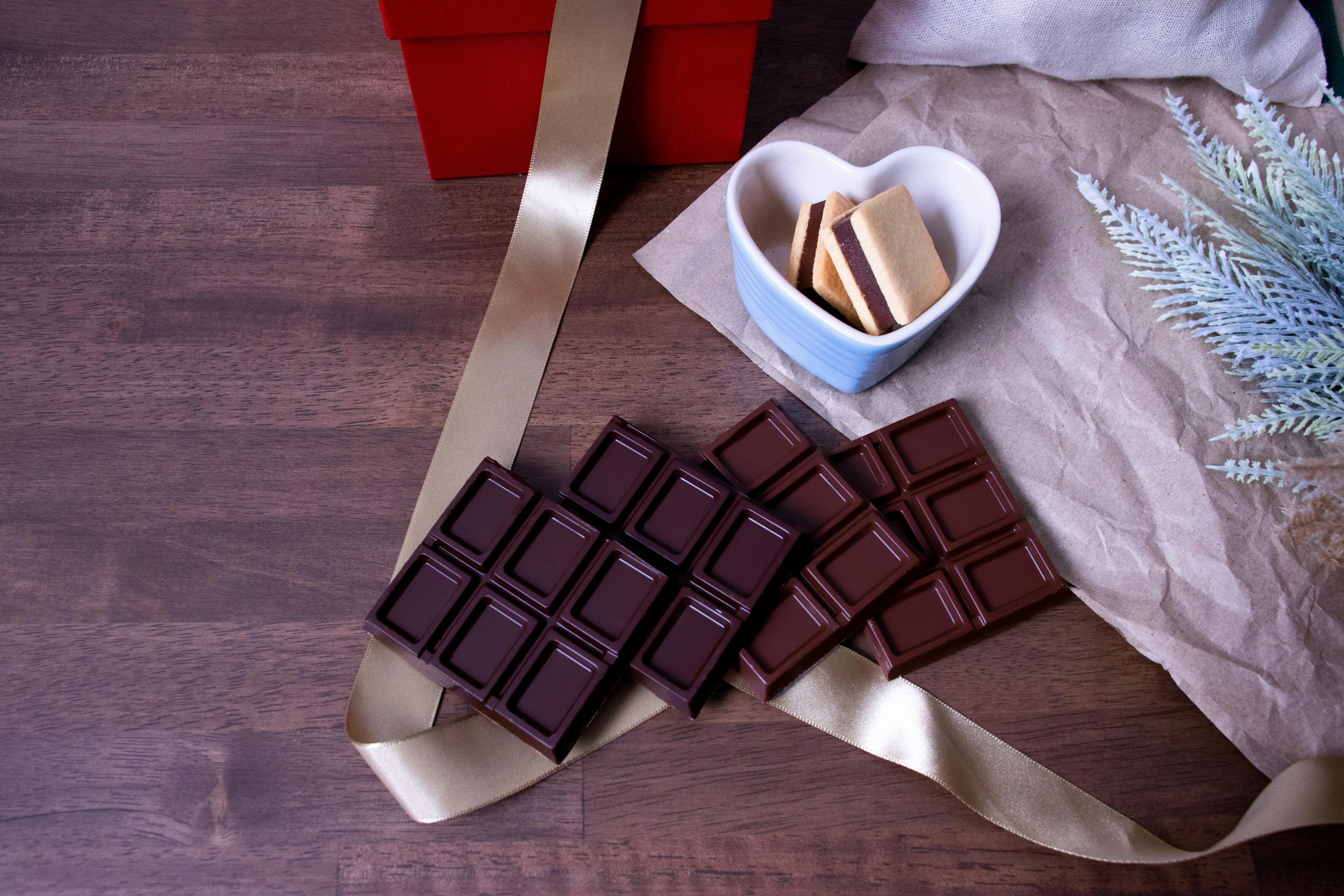 Imagen de tabletas de chocolate y galletas junto a una caja de regalo roja con un lazo dorado