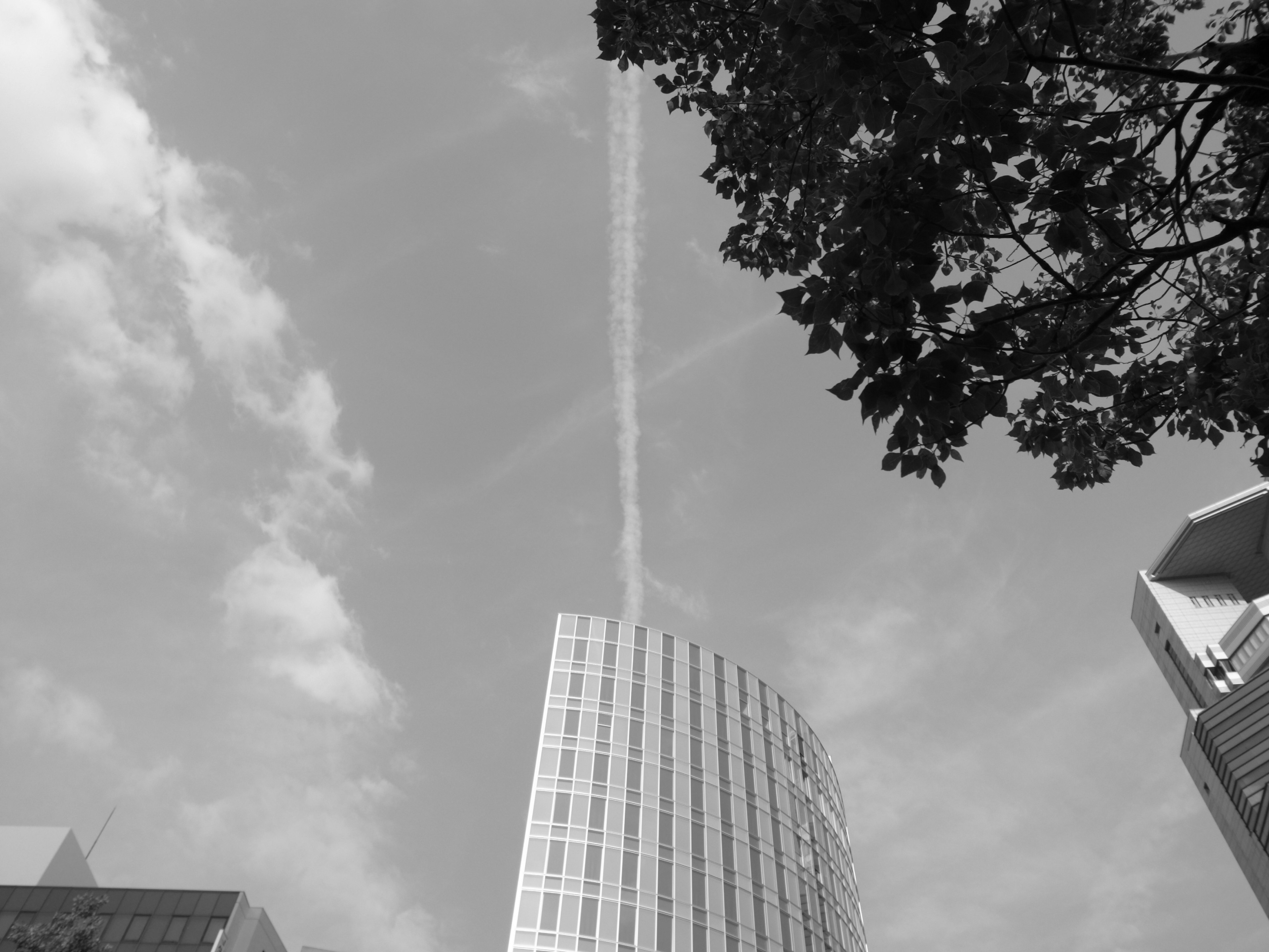 Monochrome photo of a skyscraper under blue sky and clouds with a contrail above