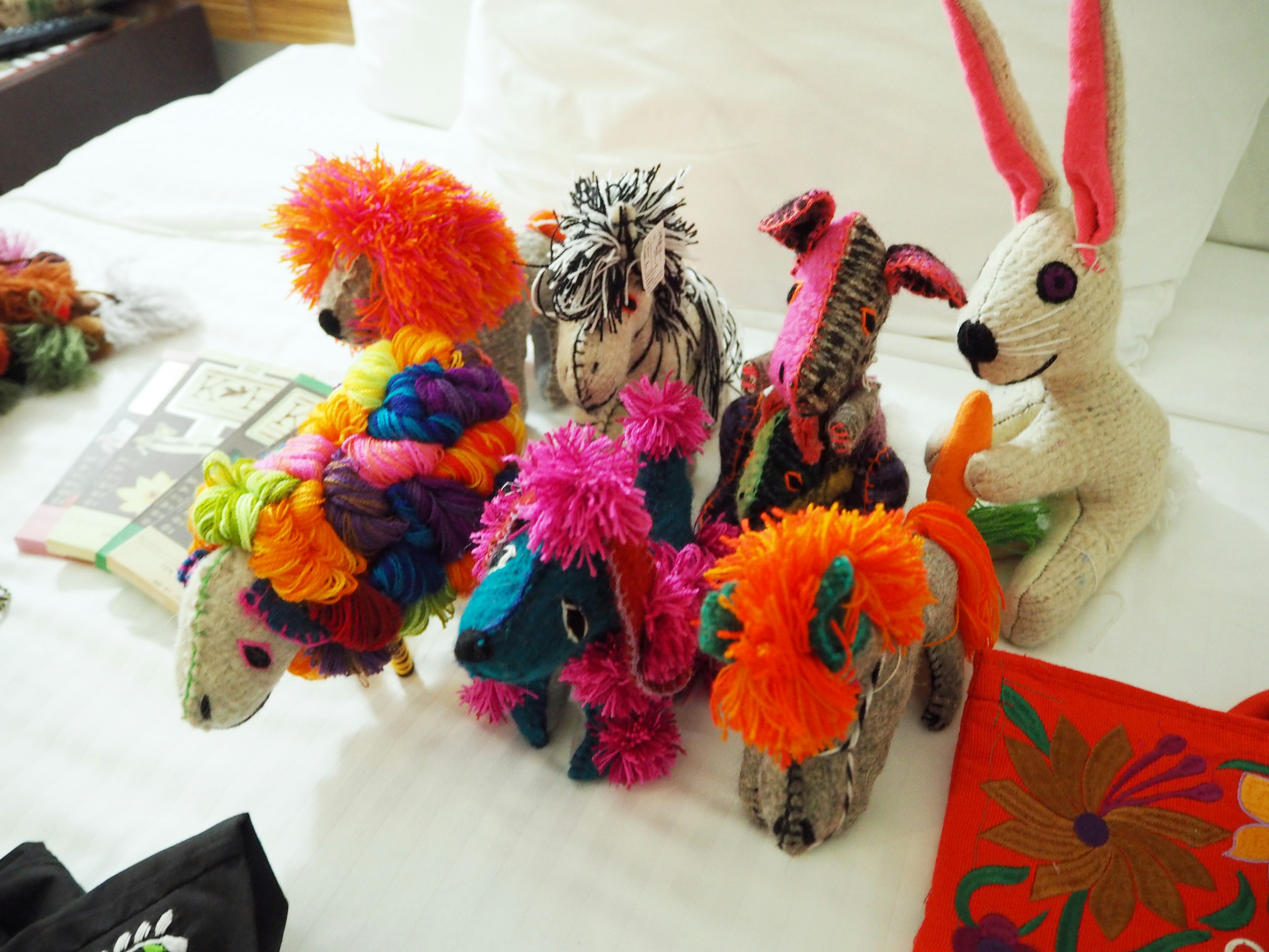 A group of colorful yarn animals arranged on a white bed