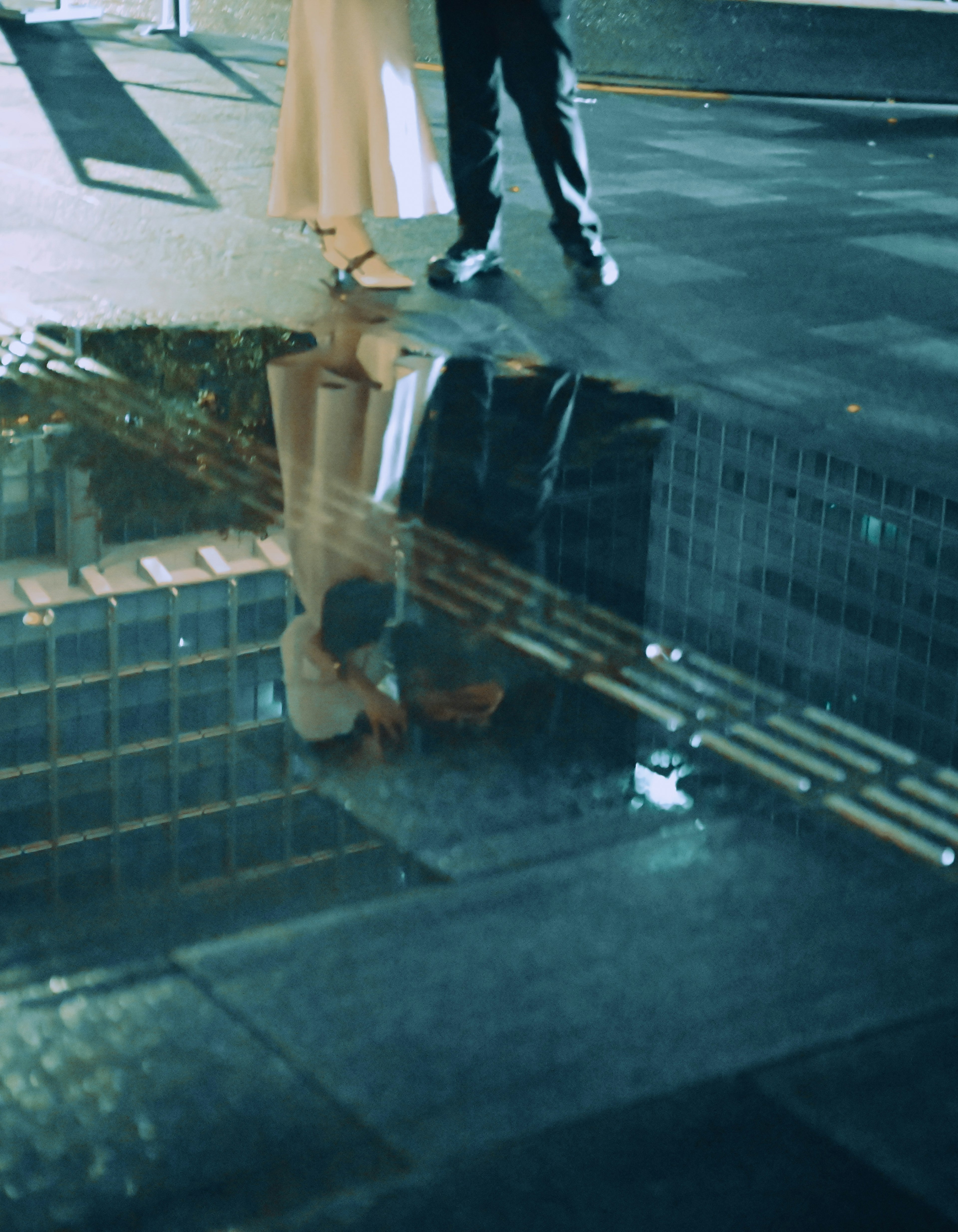 Couple's feet reflected in a puddle with urban scenery