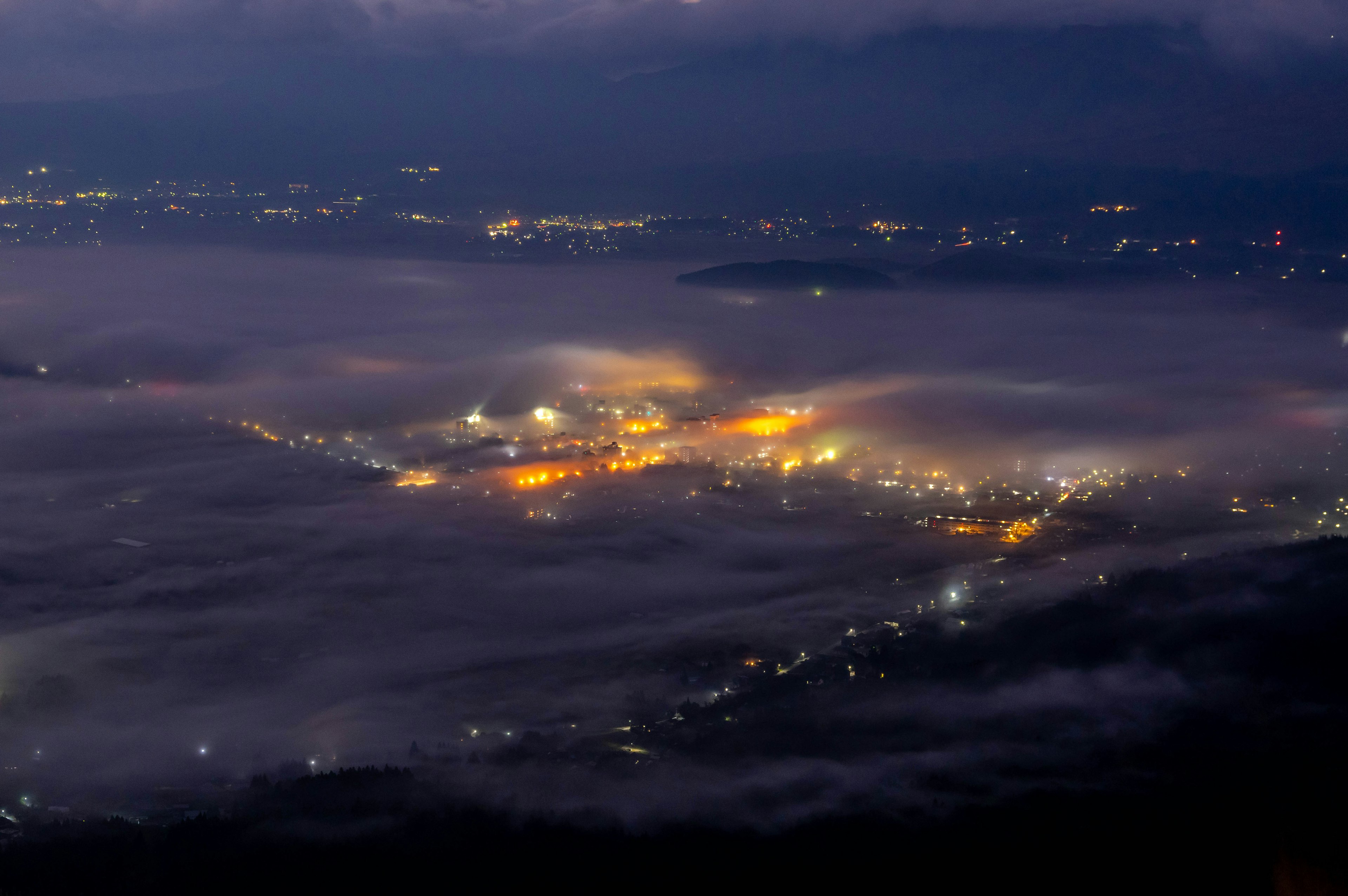 A panoramic view of an industrial area illuminated at night surrounded by fog