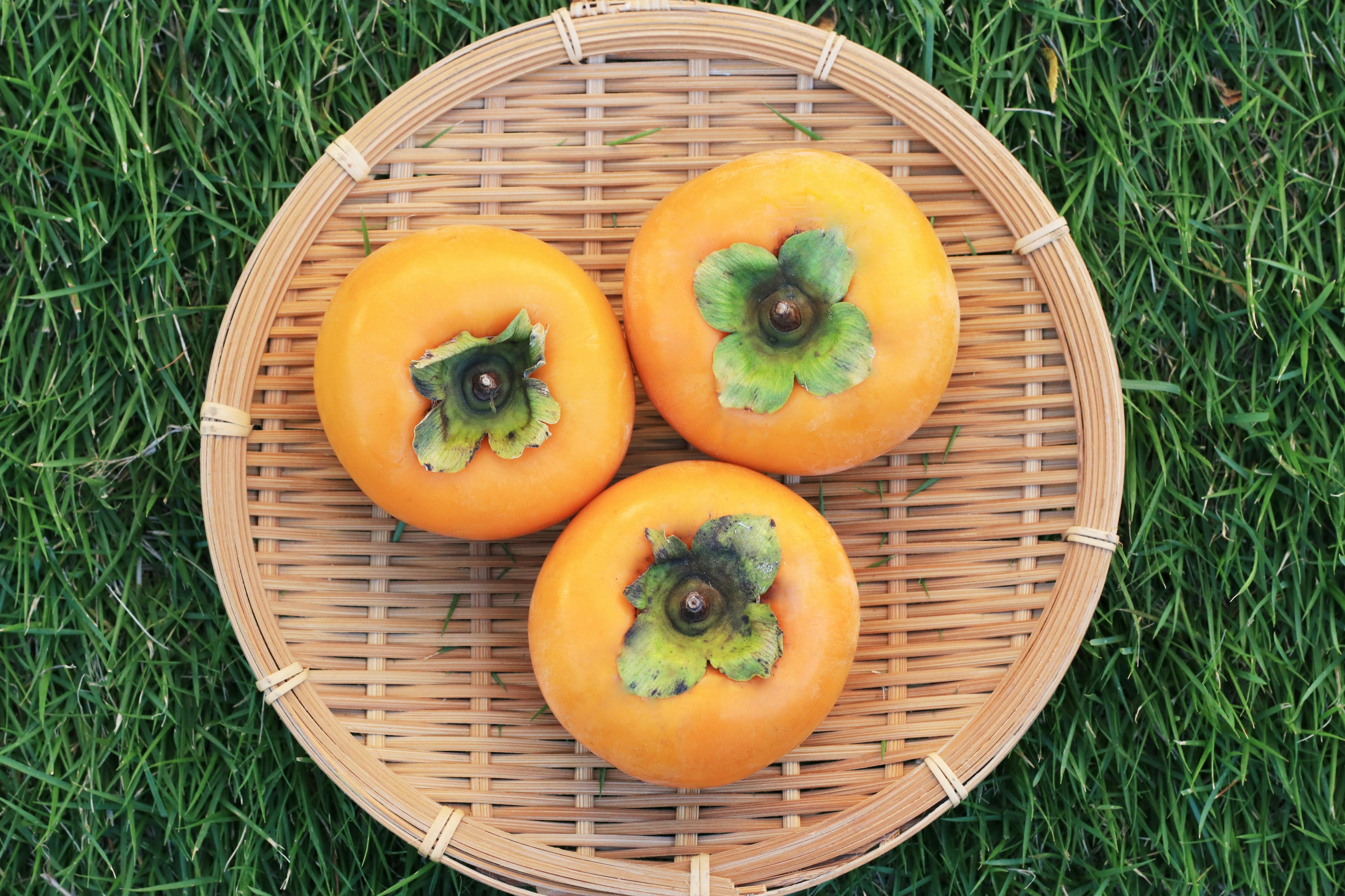 Three persimmons arranged in a bamboo basket on green grass