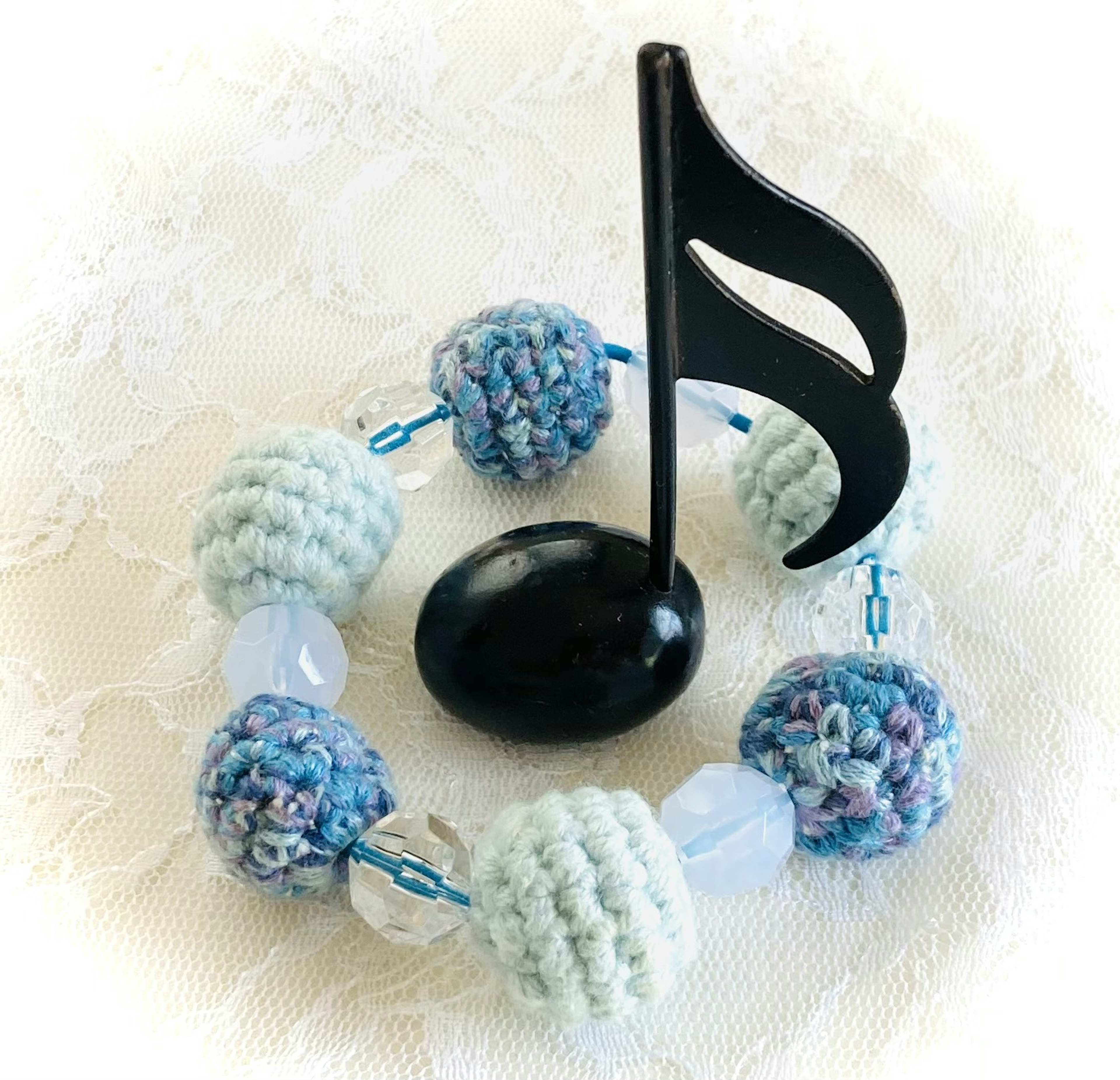 Une pièce décorative avec des perles bleues et des boules crochetées, accompagnée d'un support en forme de note de musique noire