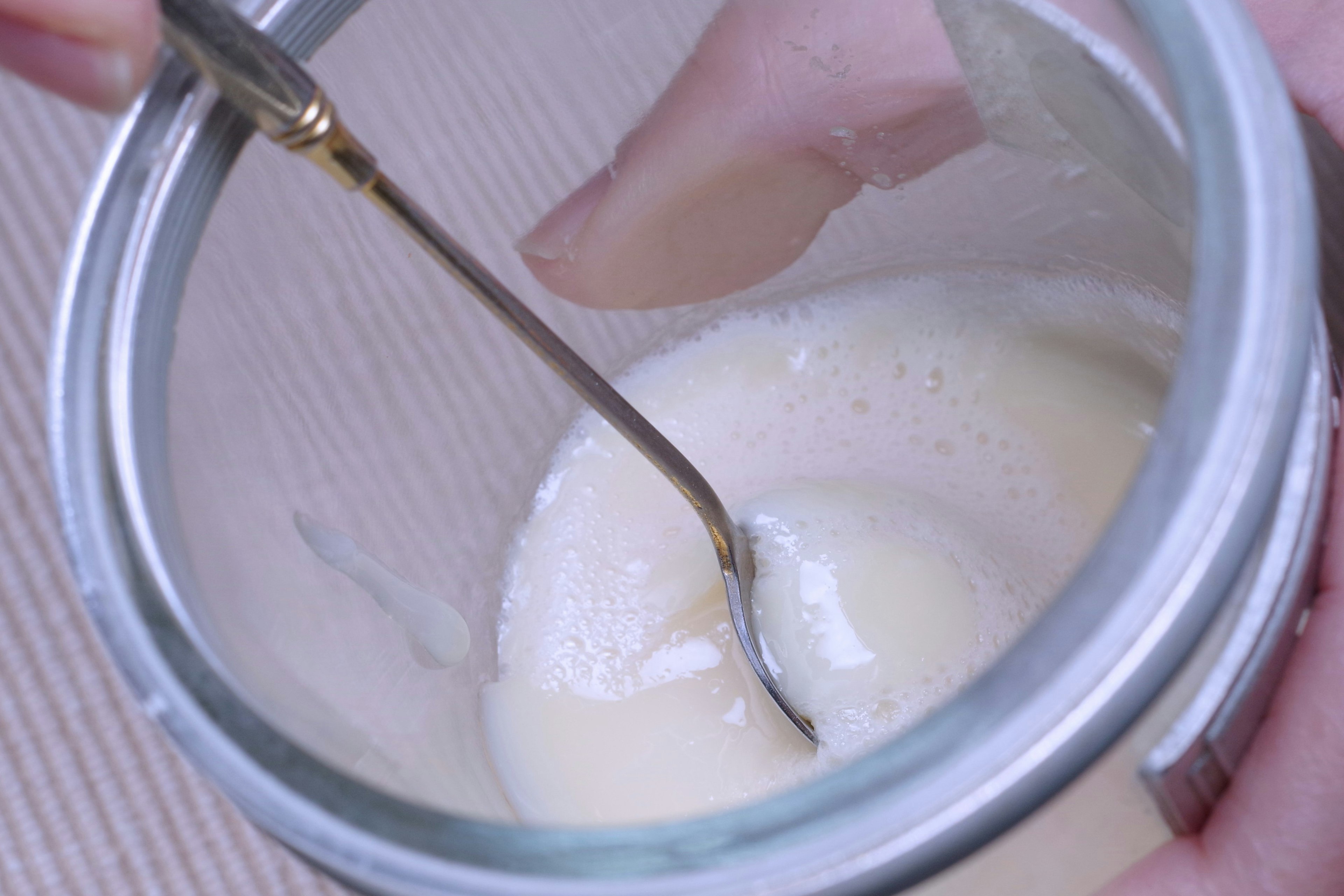 A hand stirring a creamy substance in a glass jar