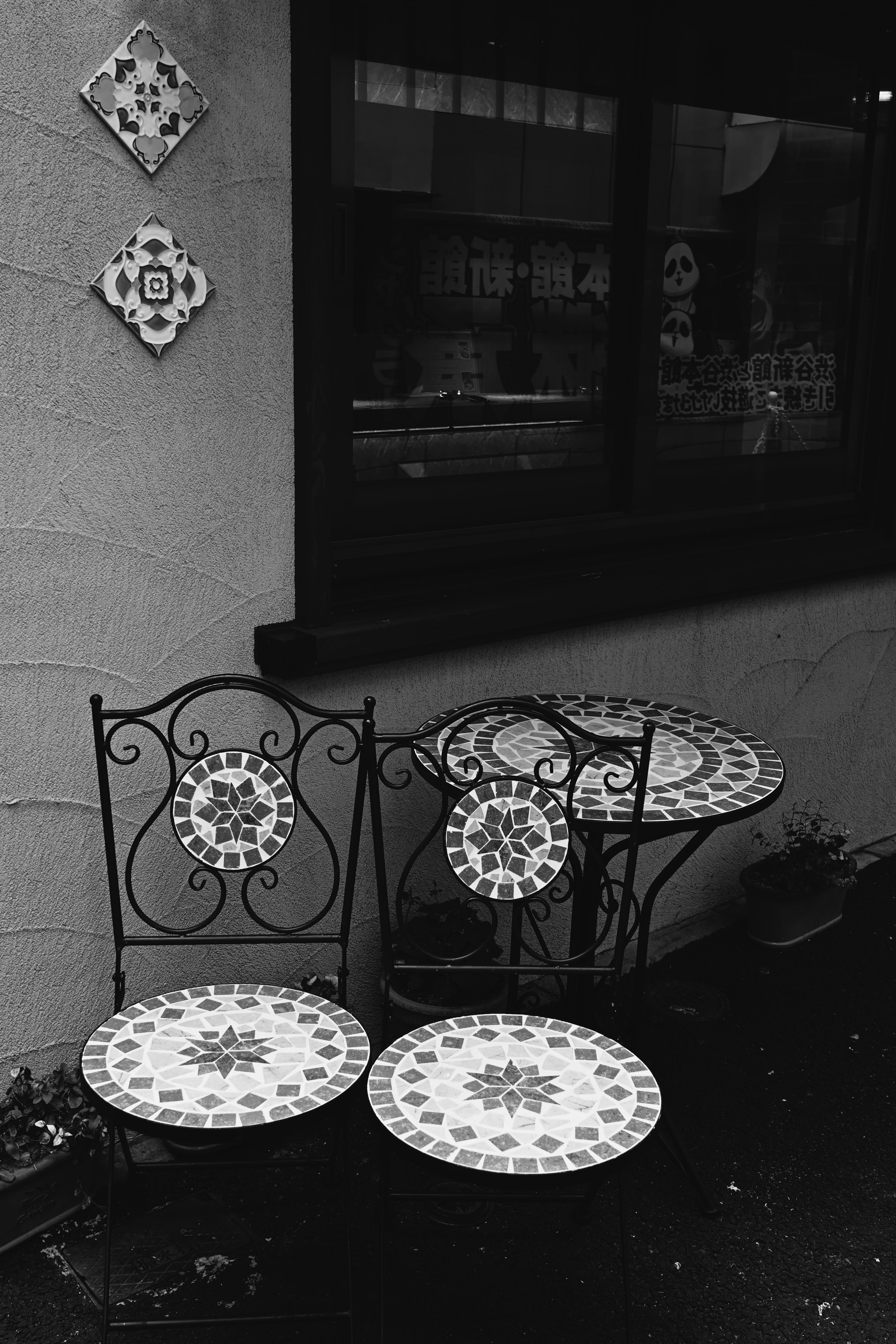 Mesa y sillas de azulejos decorativos en el exterior de un café en blanco y negro