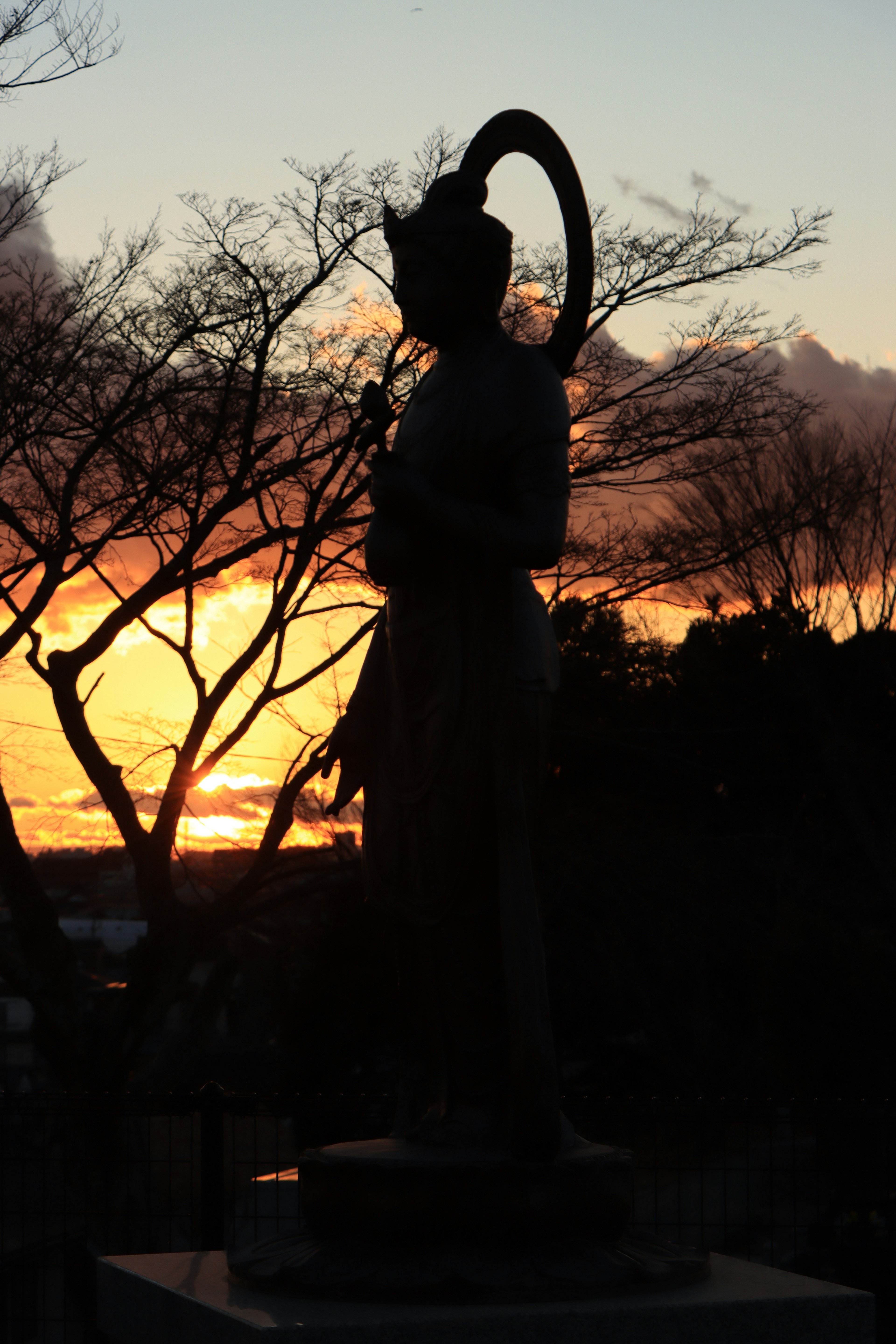 Silhouette einer Statue vor einem Sonnenuntergang mit Bäumen im Hintergrund