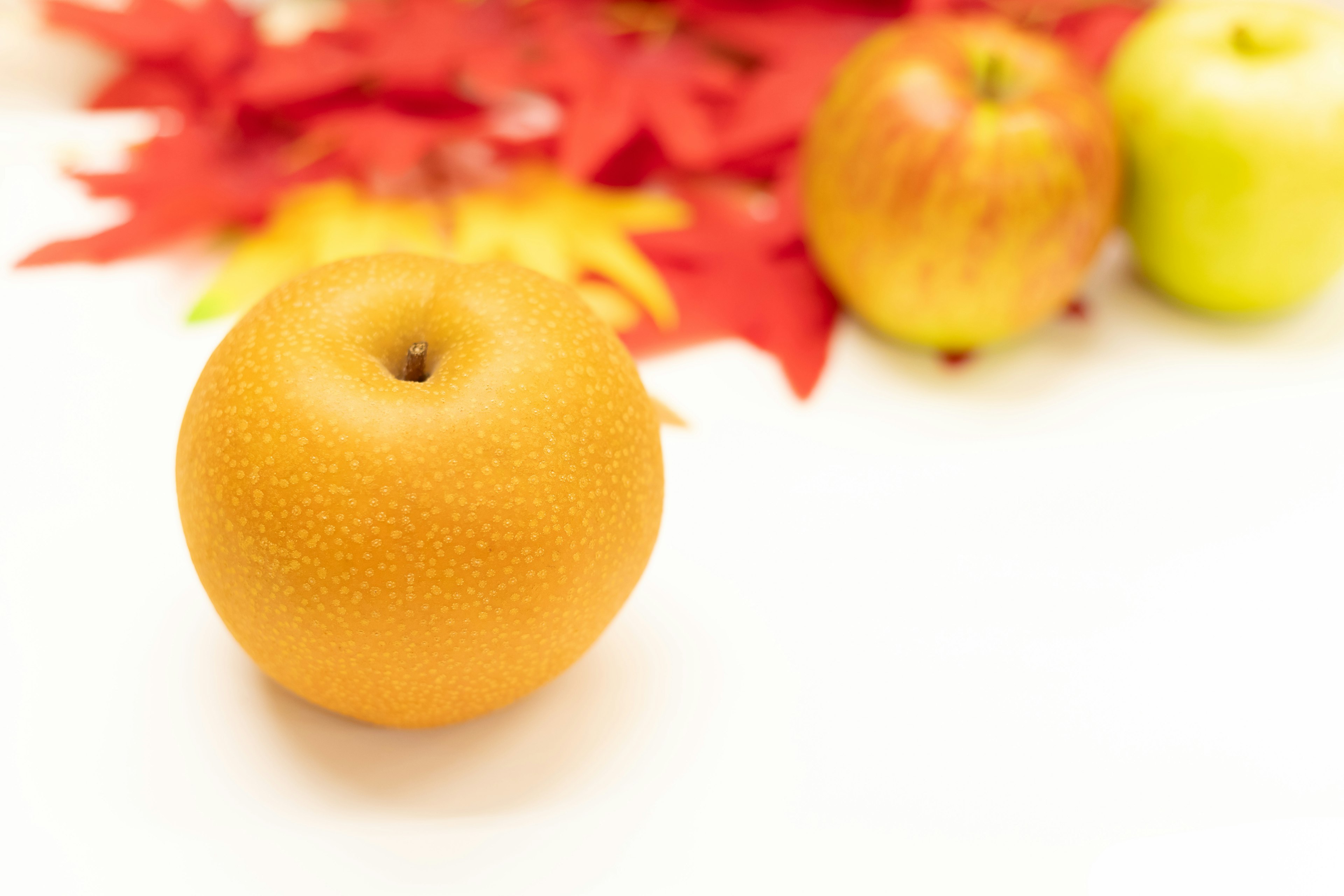 An orange pear in the foreground with red leaves and apples in the background