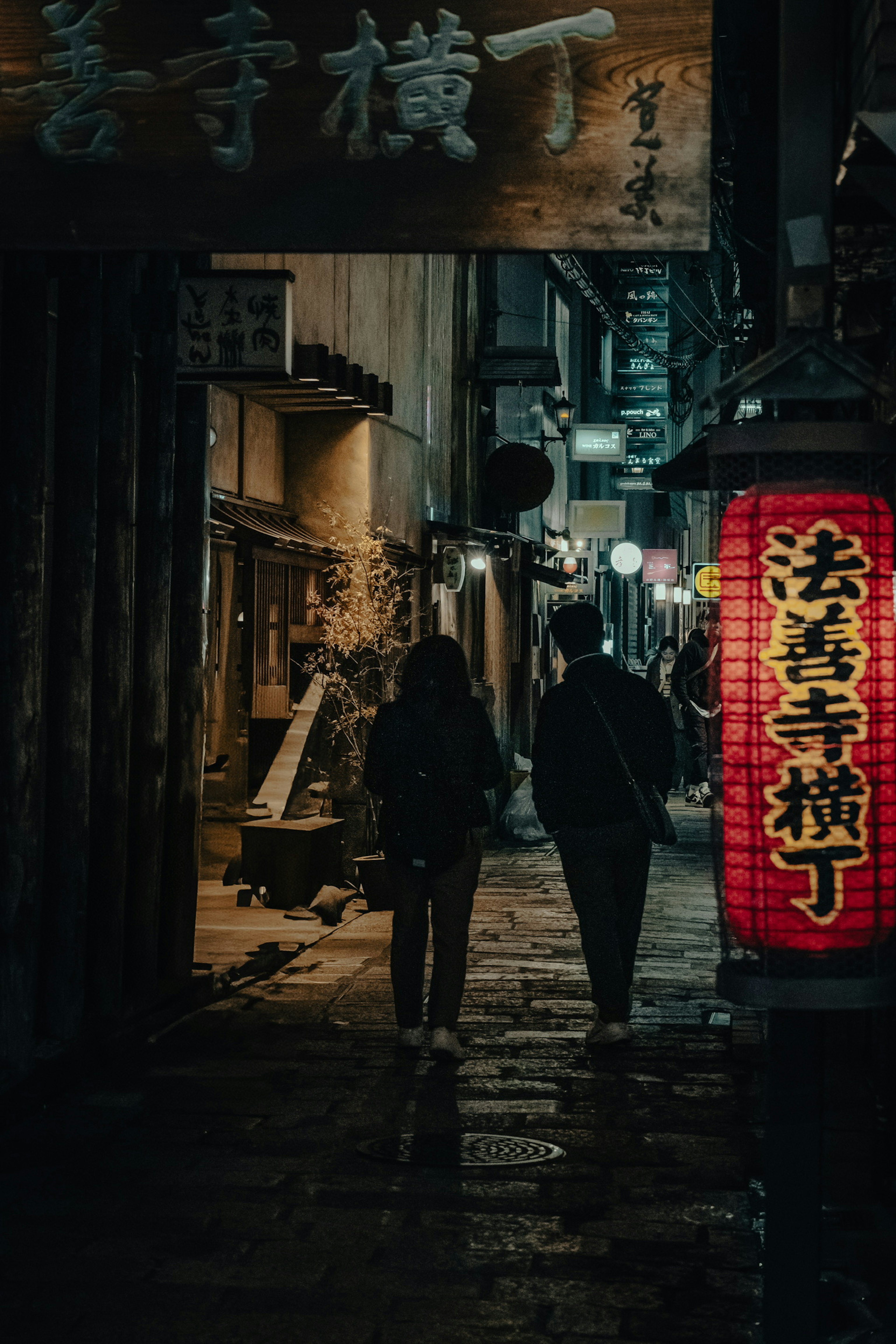 Personas caminando en un callejón oscuro iluminado por una linterna roja