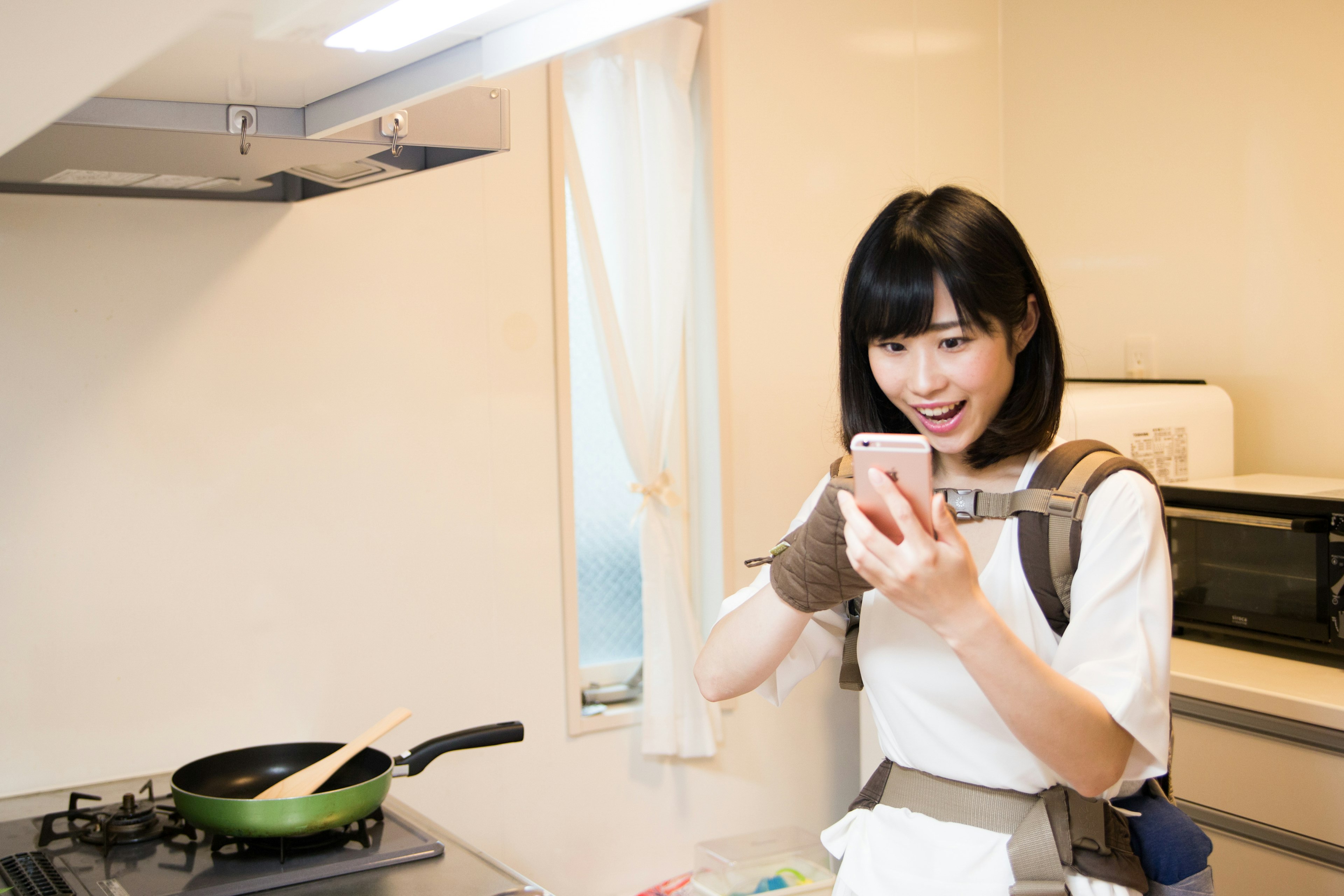 Woman in a kitchen holding a smartphone and looking surprised