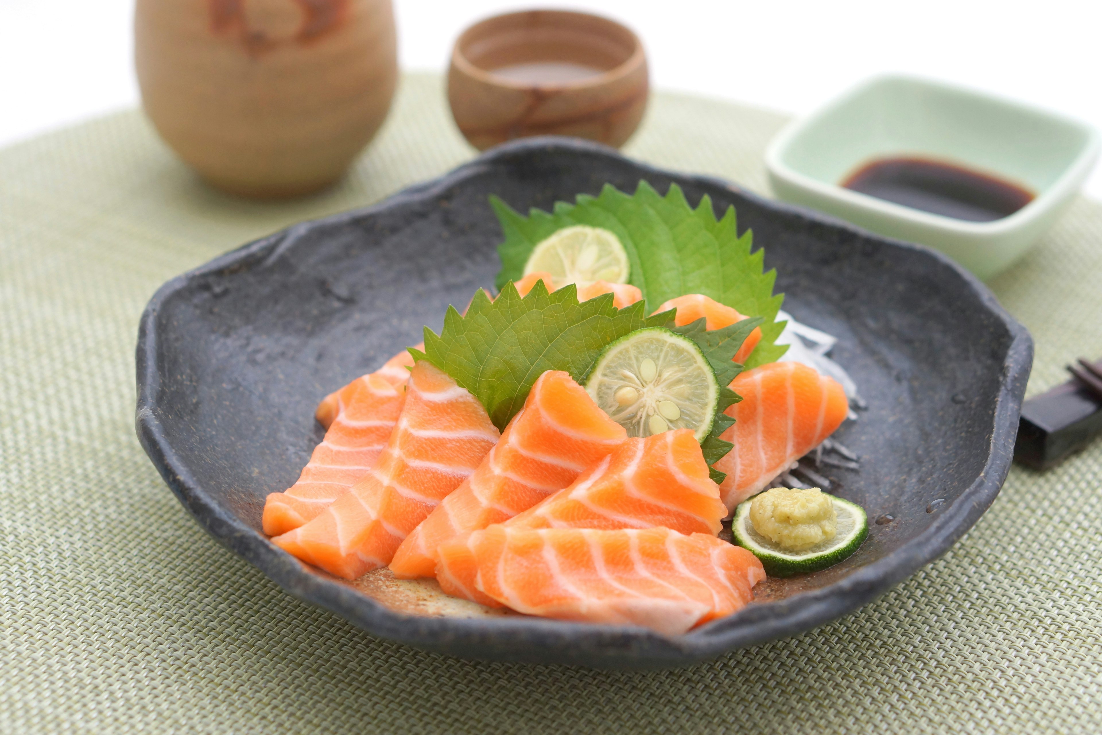 Sashimi di salmone fresco disposto su un piatto nero con fette di lime