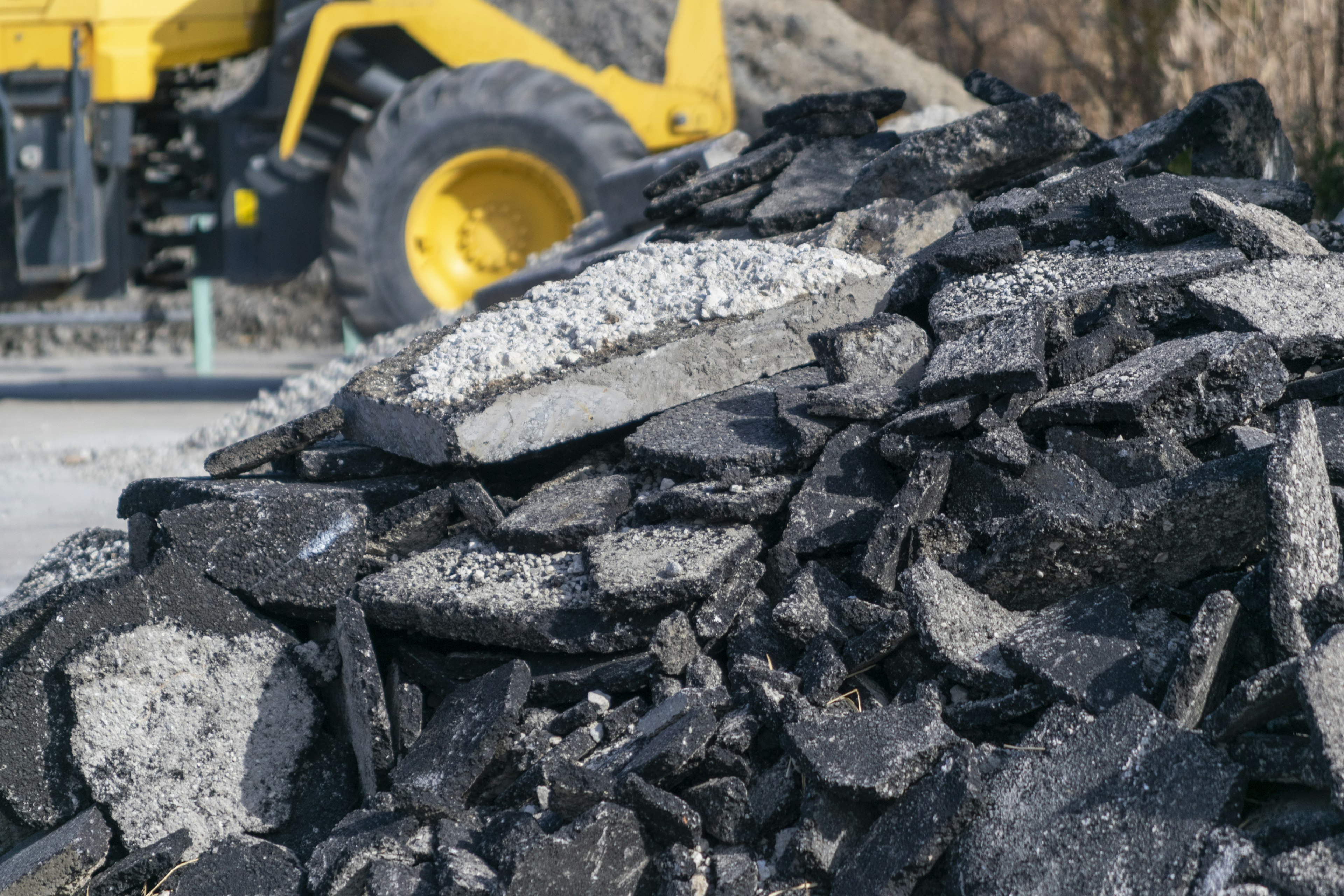 Piled asphalt rubble with a yellow construction vehicle in the background