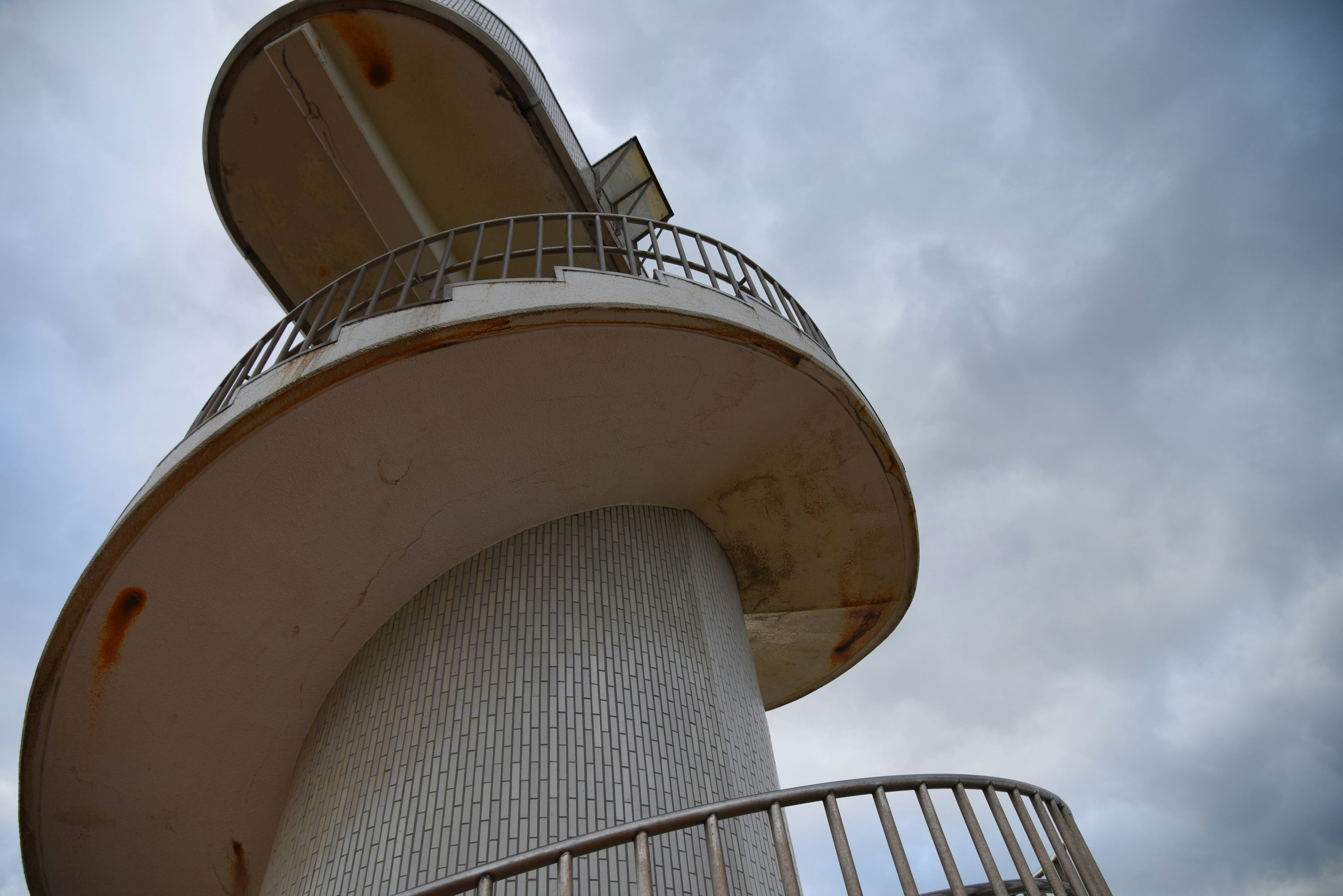 Photo of a white lighthouse with a spiral staircase under a cloudy sky