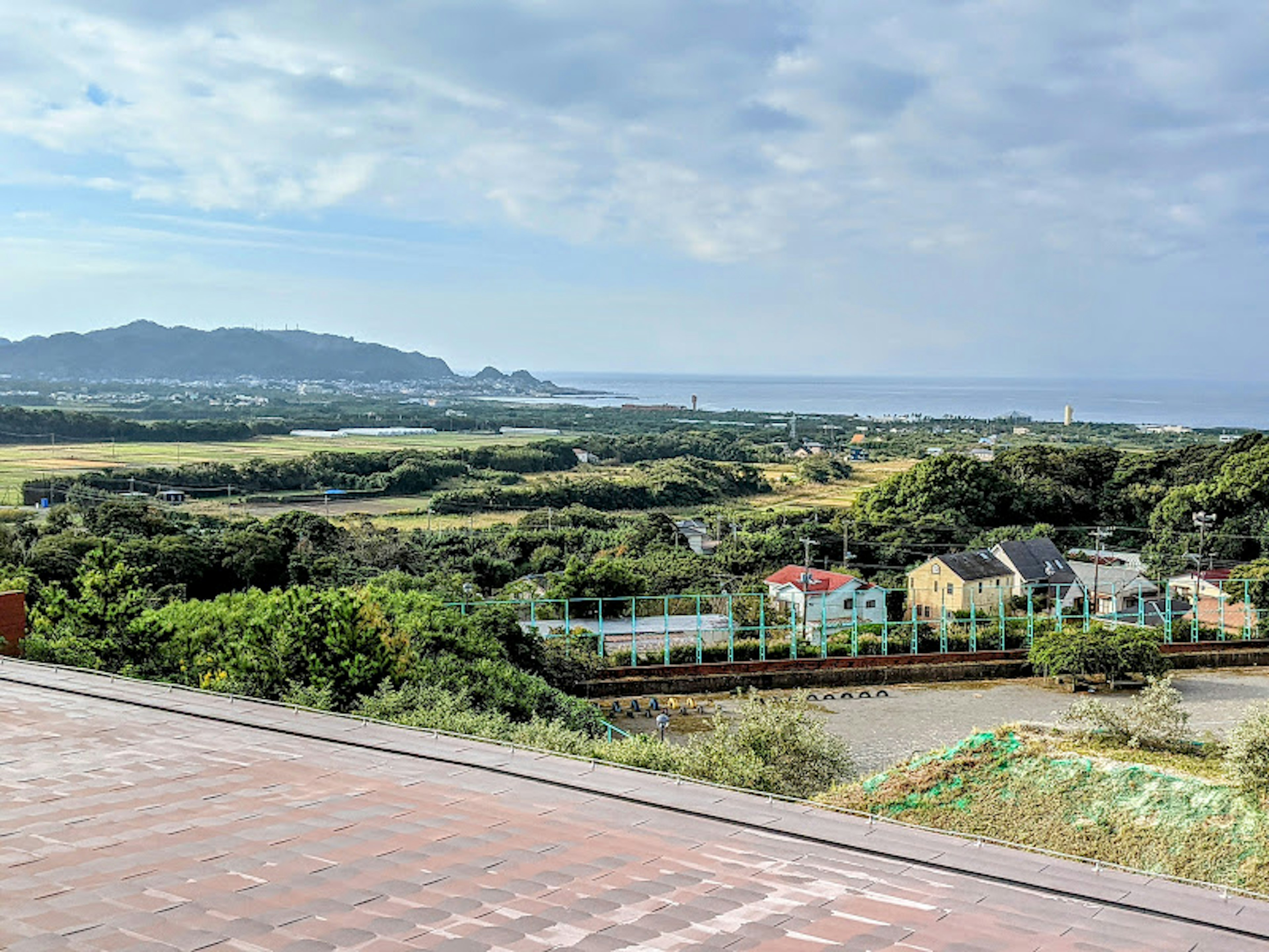 Scenic view of green hills and houses with mountains and ocean in the background