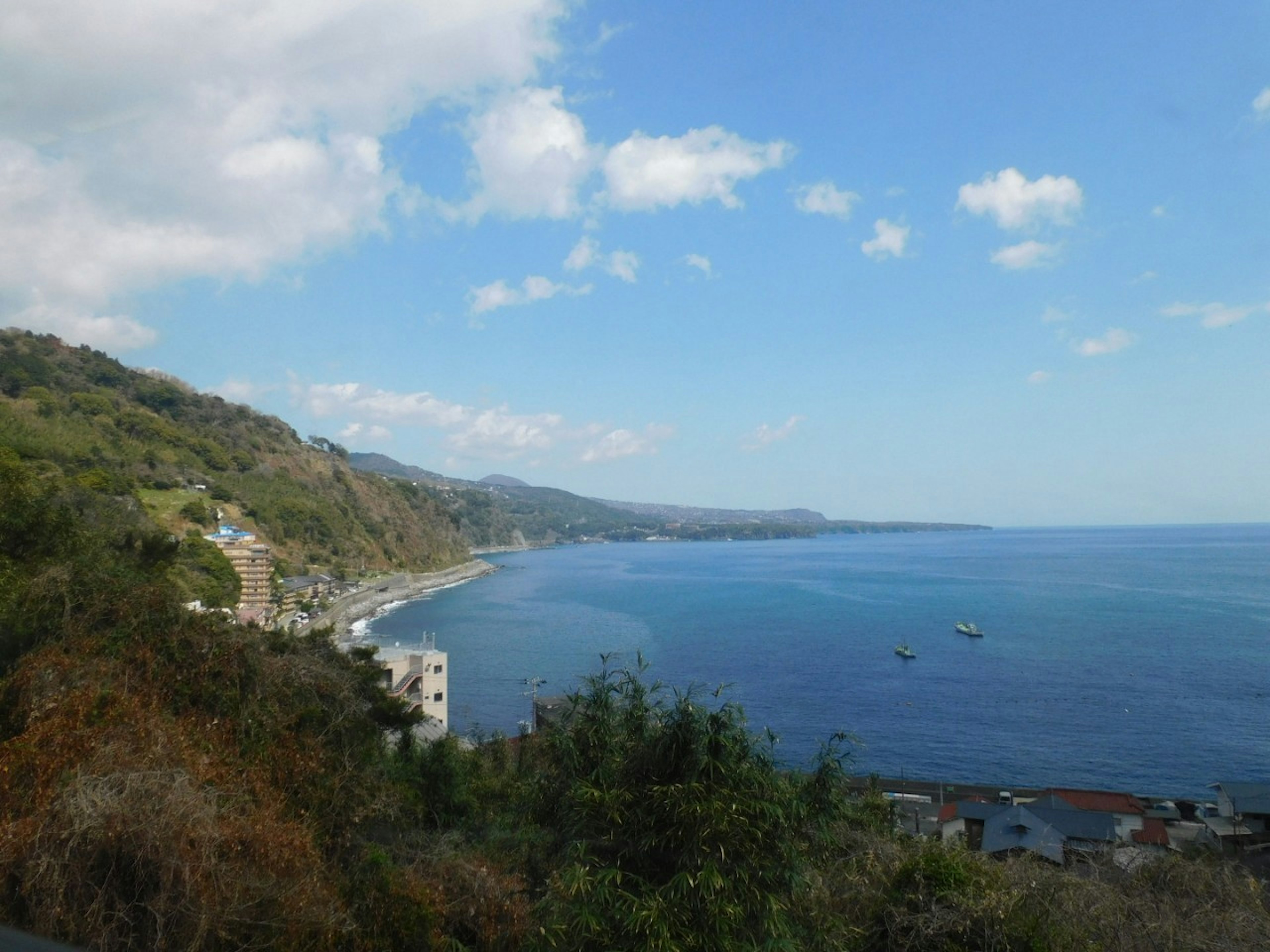 Scenic view of blue sea and green hills under a partly cloudy sky