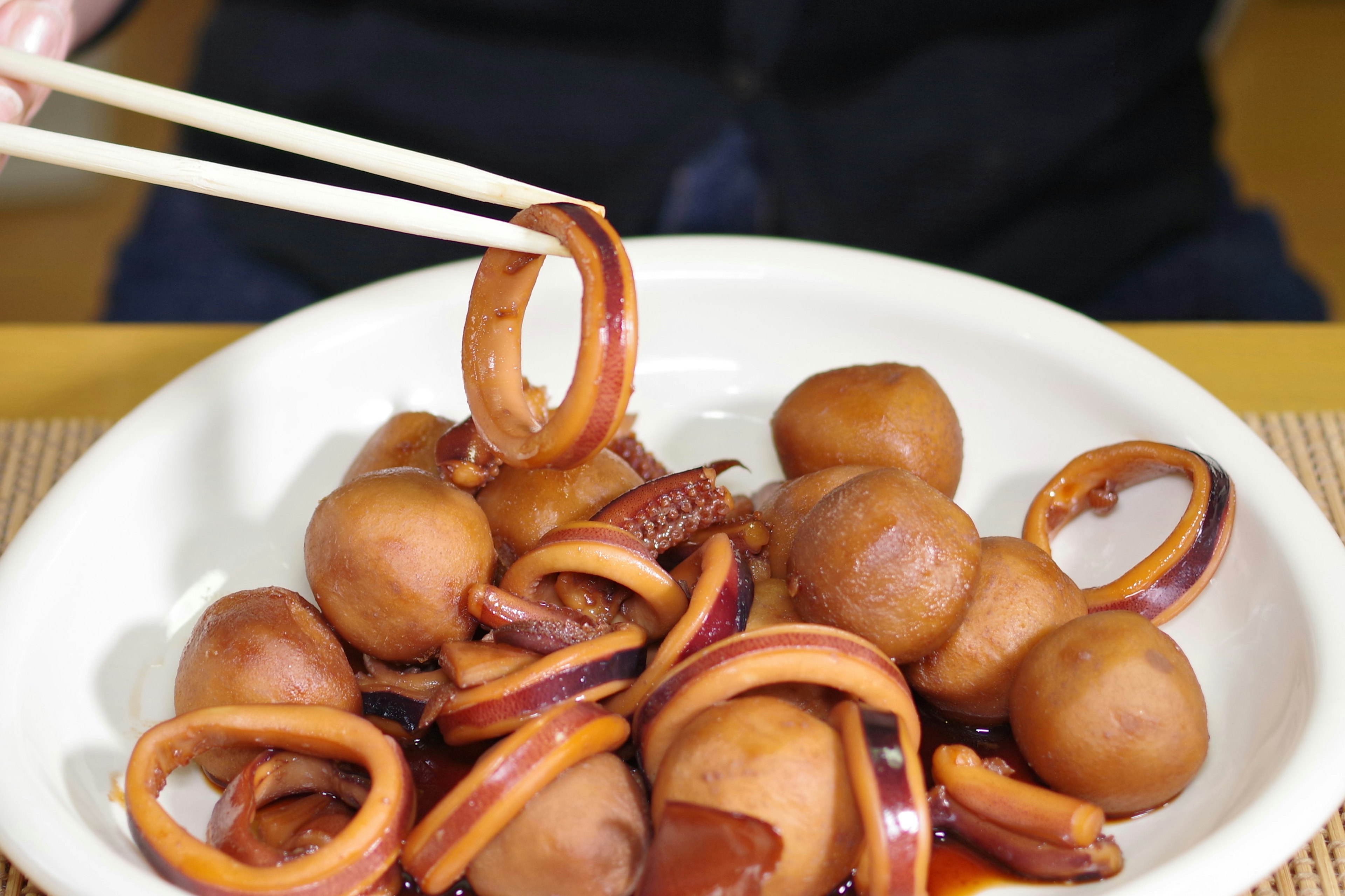 A hand using chopsticks to pick up squid rings and round ingredients on a plate