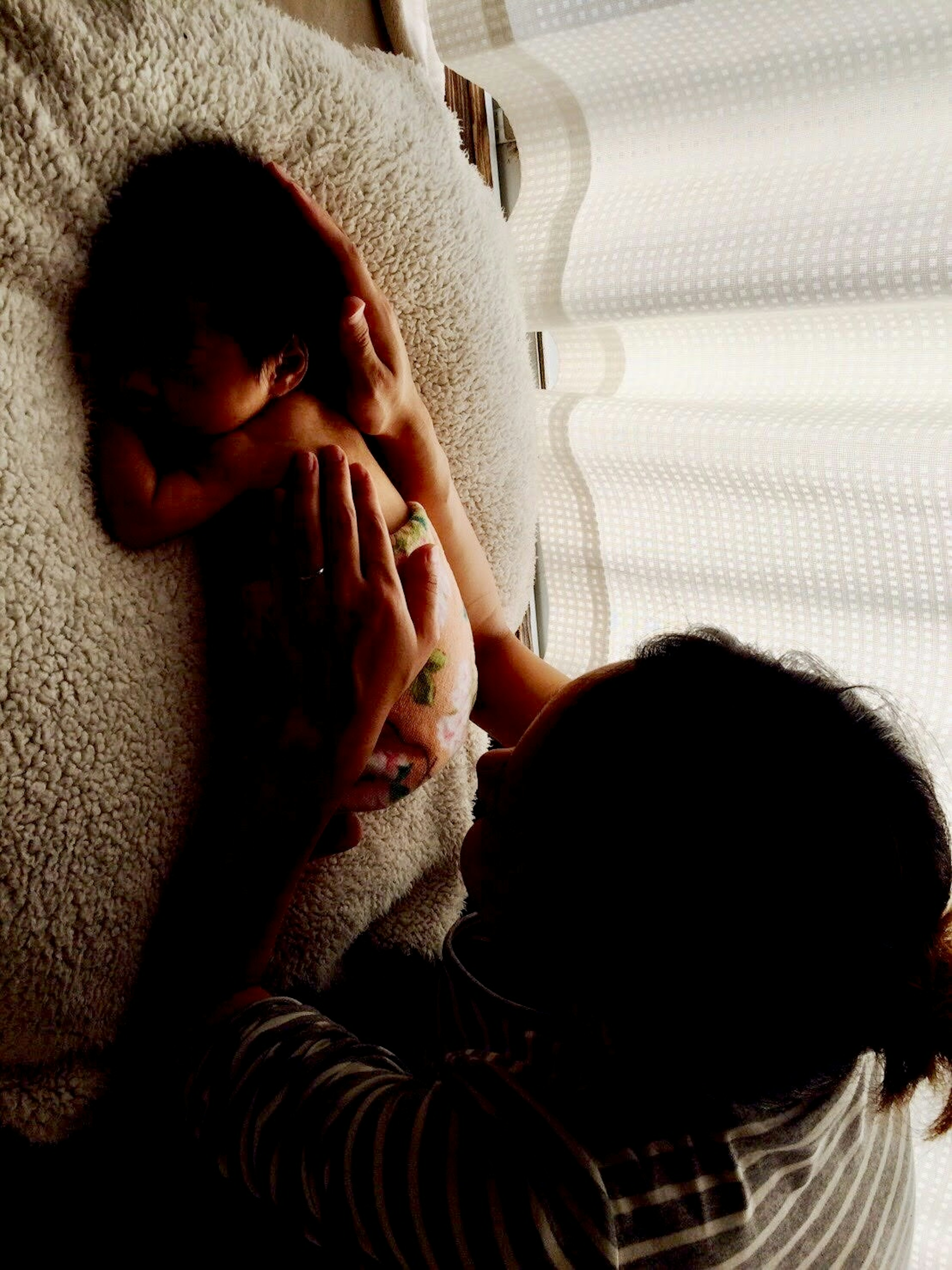 Silhouette einer Mutter, die ein Baby auf einer weichen Decke massiert