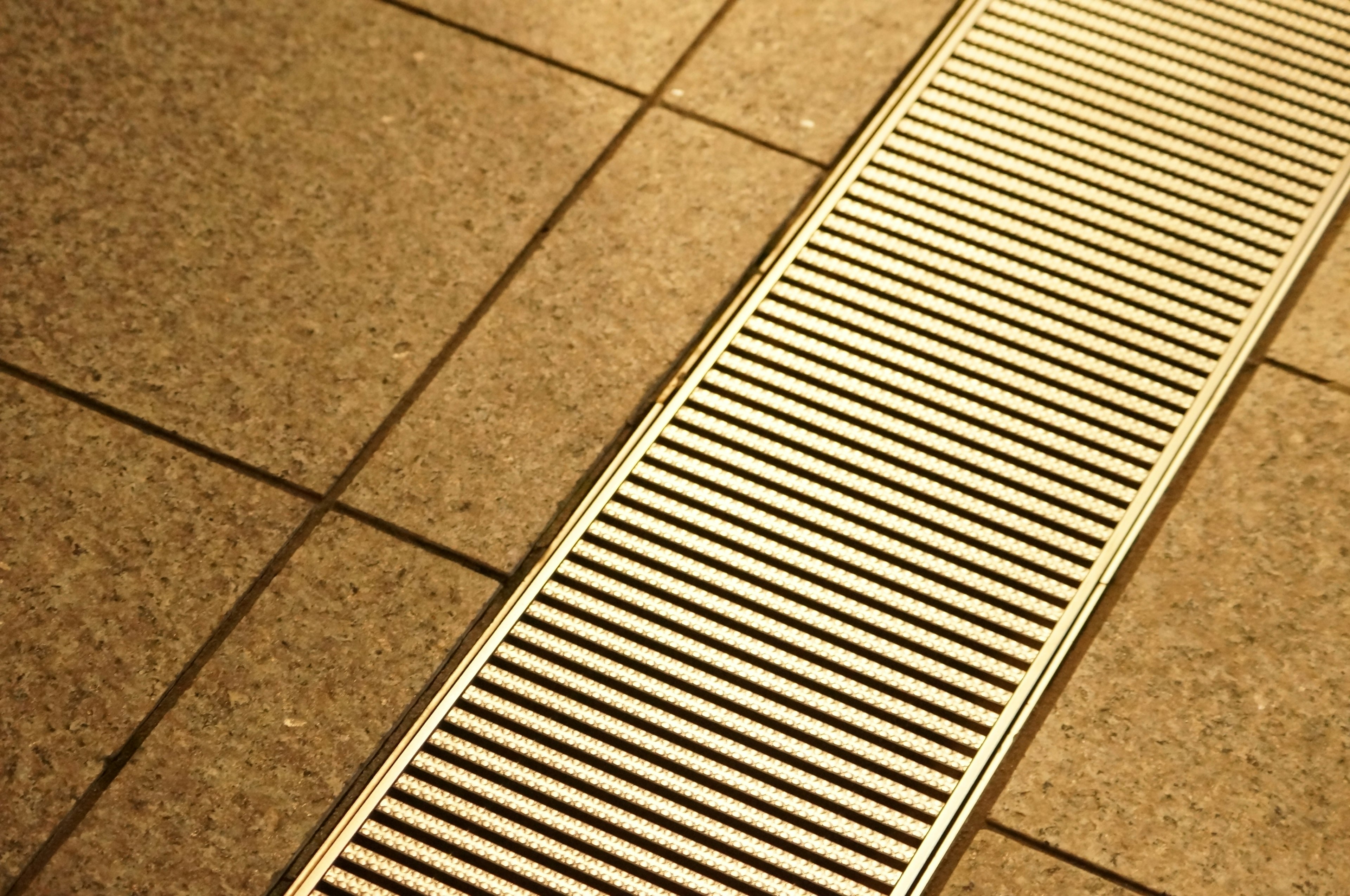 Grille de ventilation en métal installée dans le sol montrant la texture et la couleur des carreaux environnants