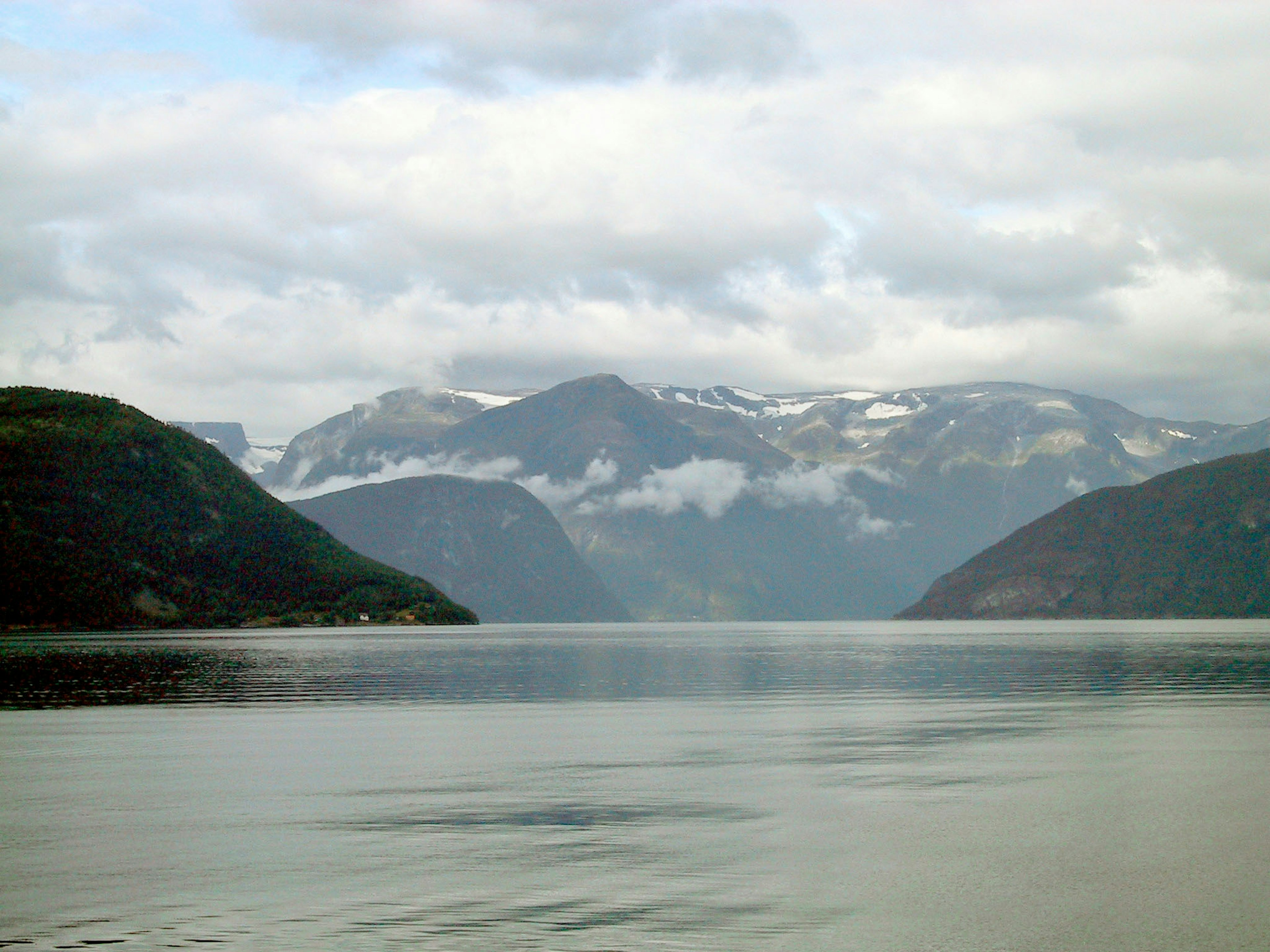 Lago calmo con montagne sullo sfondo Cielo nuvoloso con cime innevate