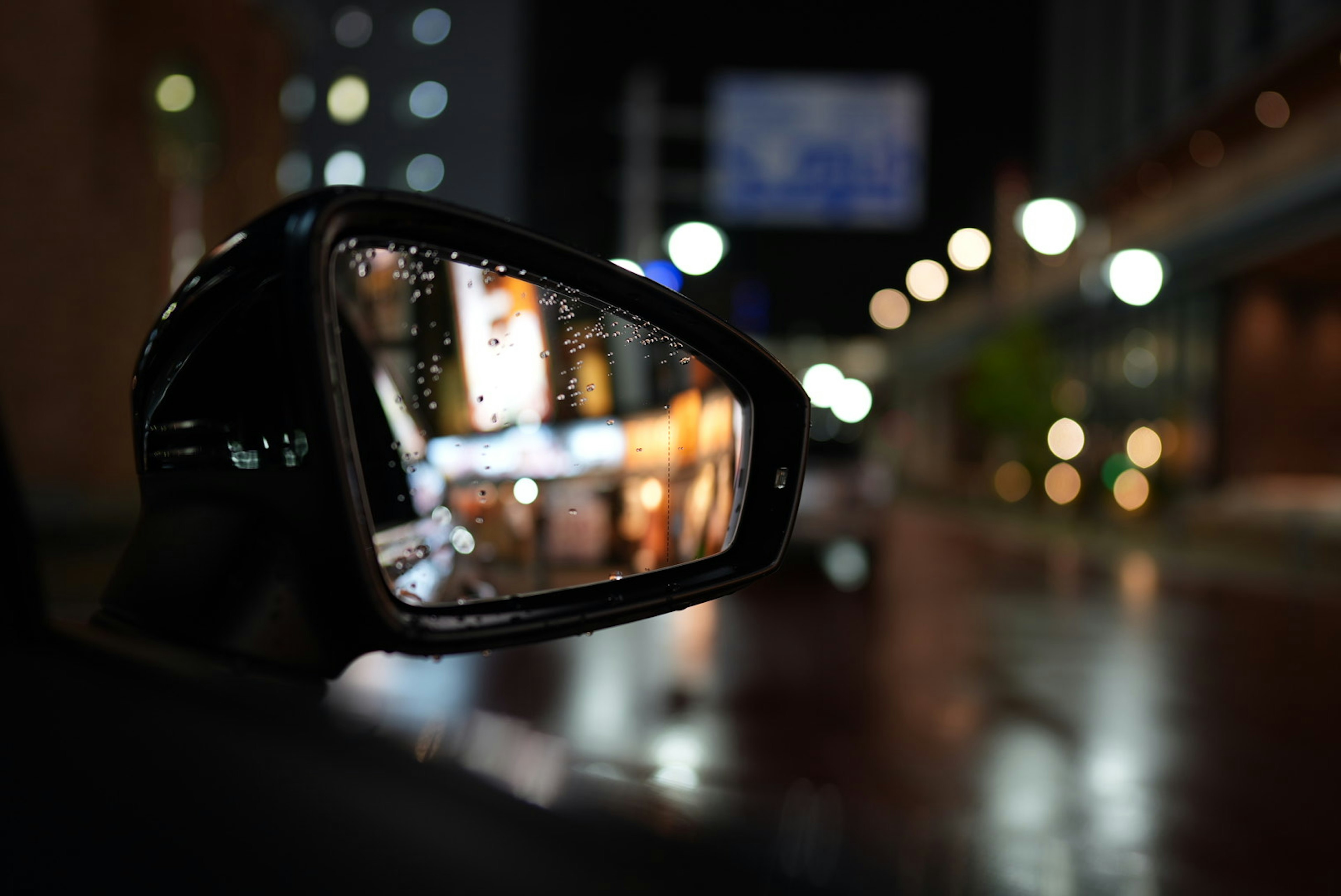 Rétroviseur de voiture reflétant les lumières de la ville la nuit avec des gouttes de pluie