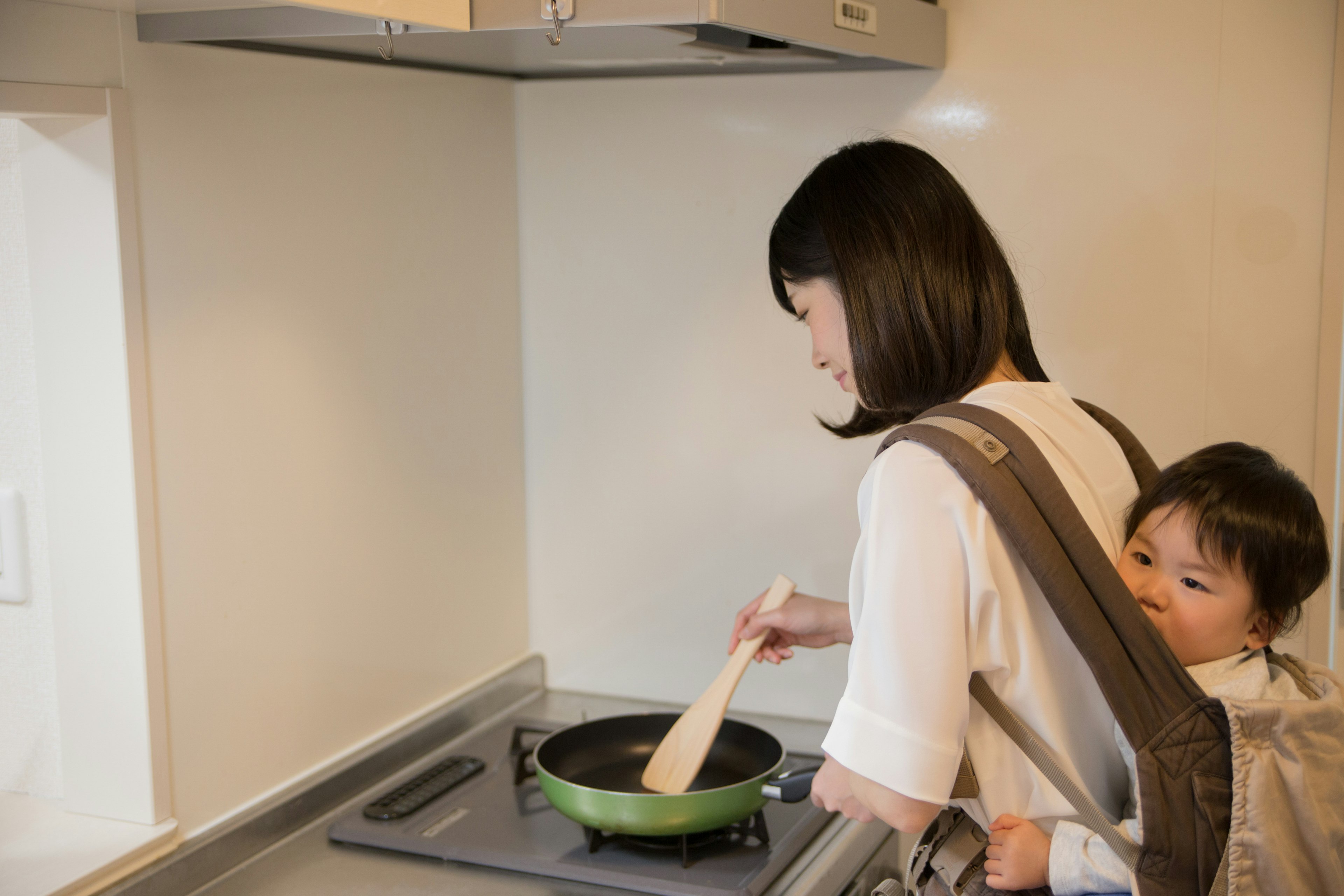 Donna che cucina con un bambino sulla schiena in una cucina moderna