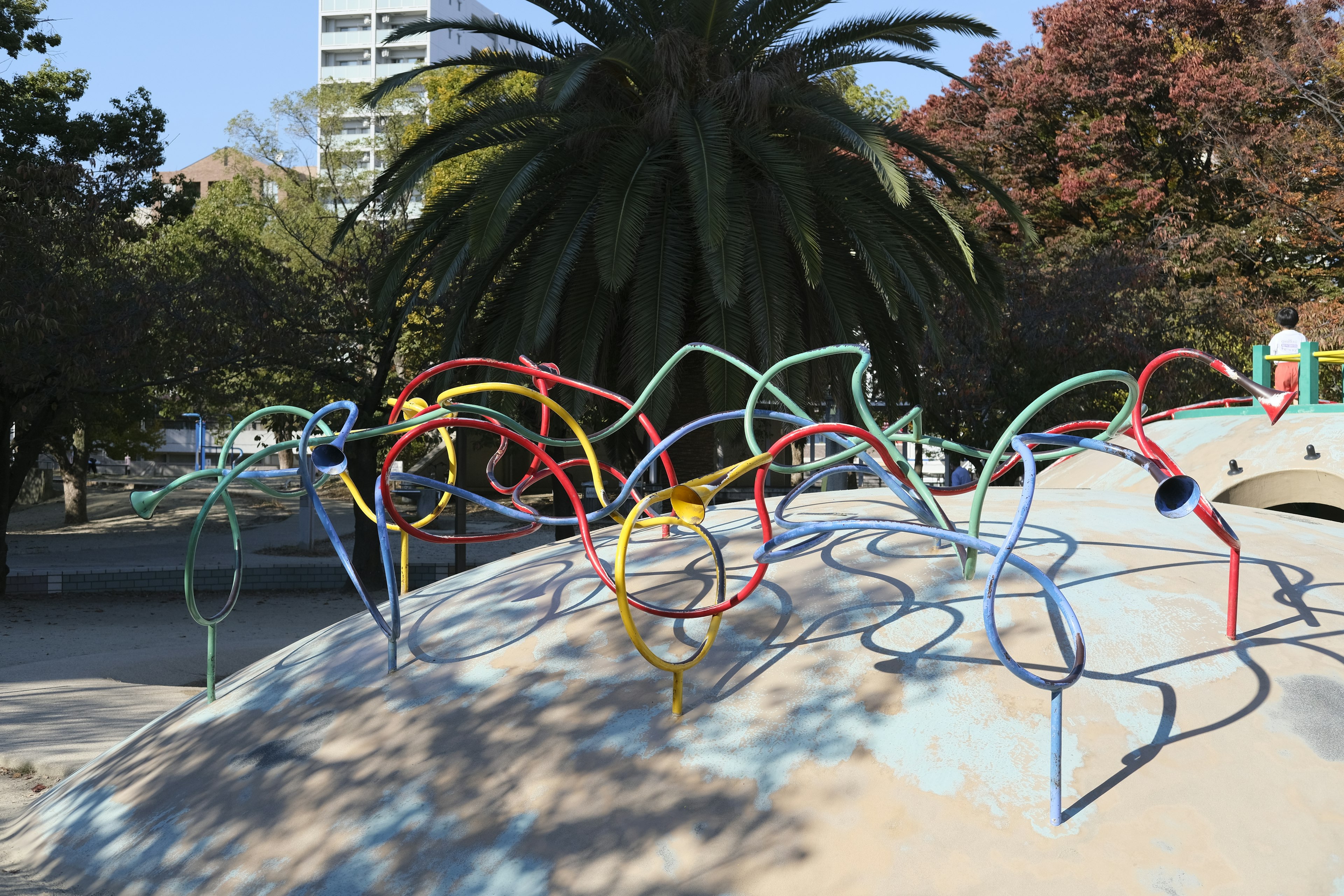 Colorful twisted metal rods on a playground structure with a palm tree in the background