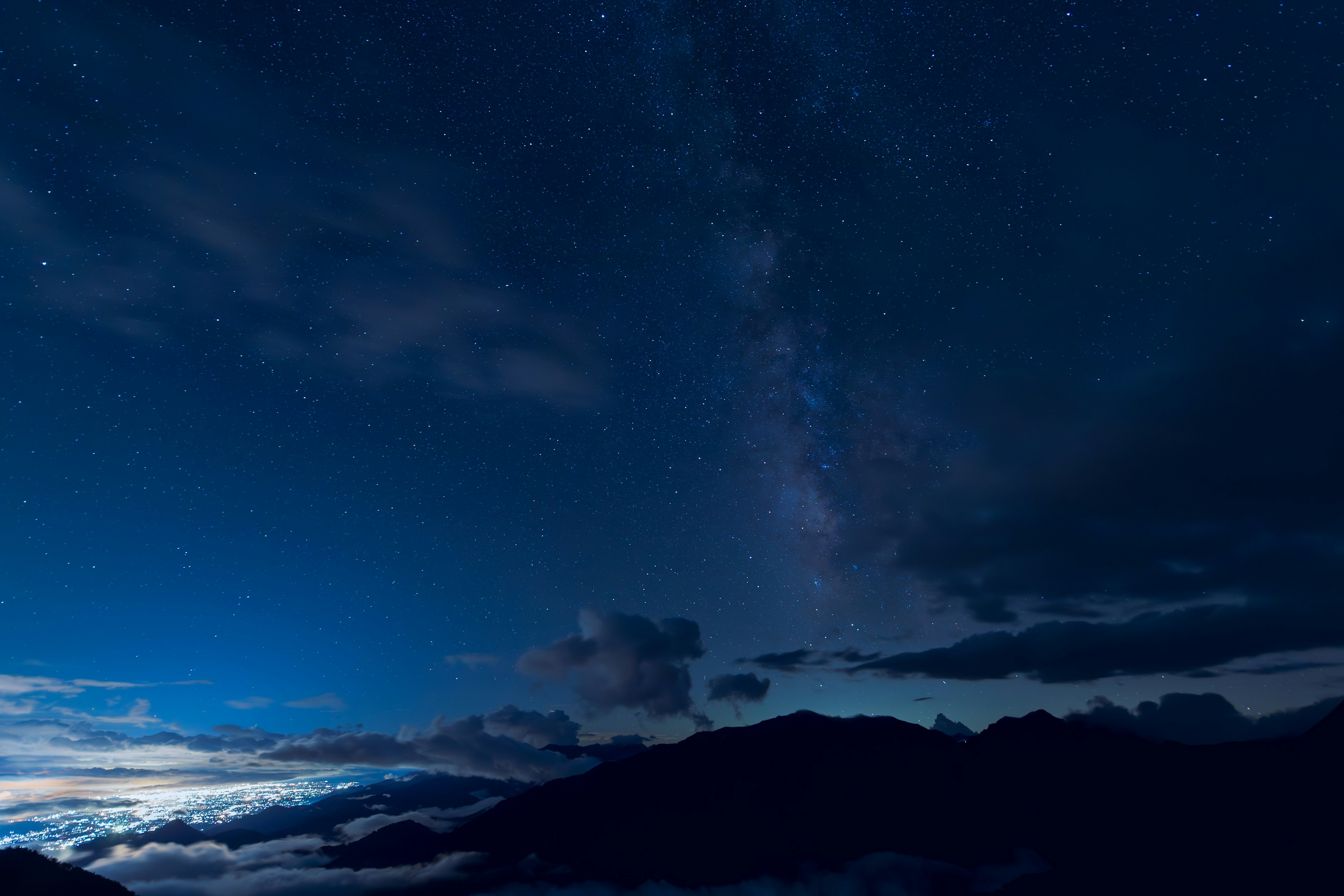 Silhouette gunung di bawah langit berbintang dengan awan