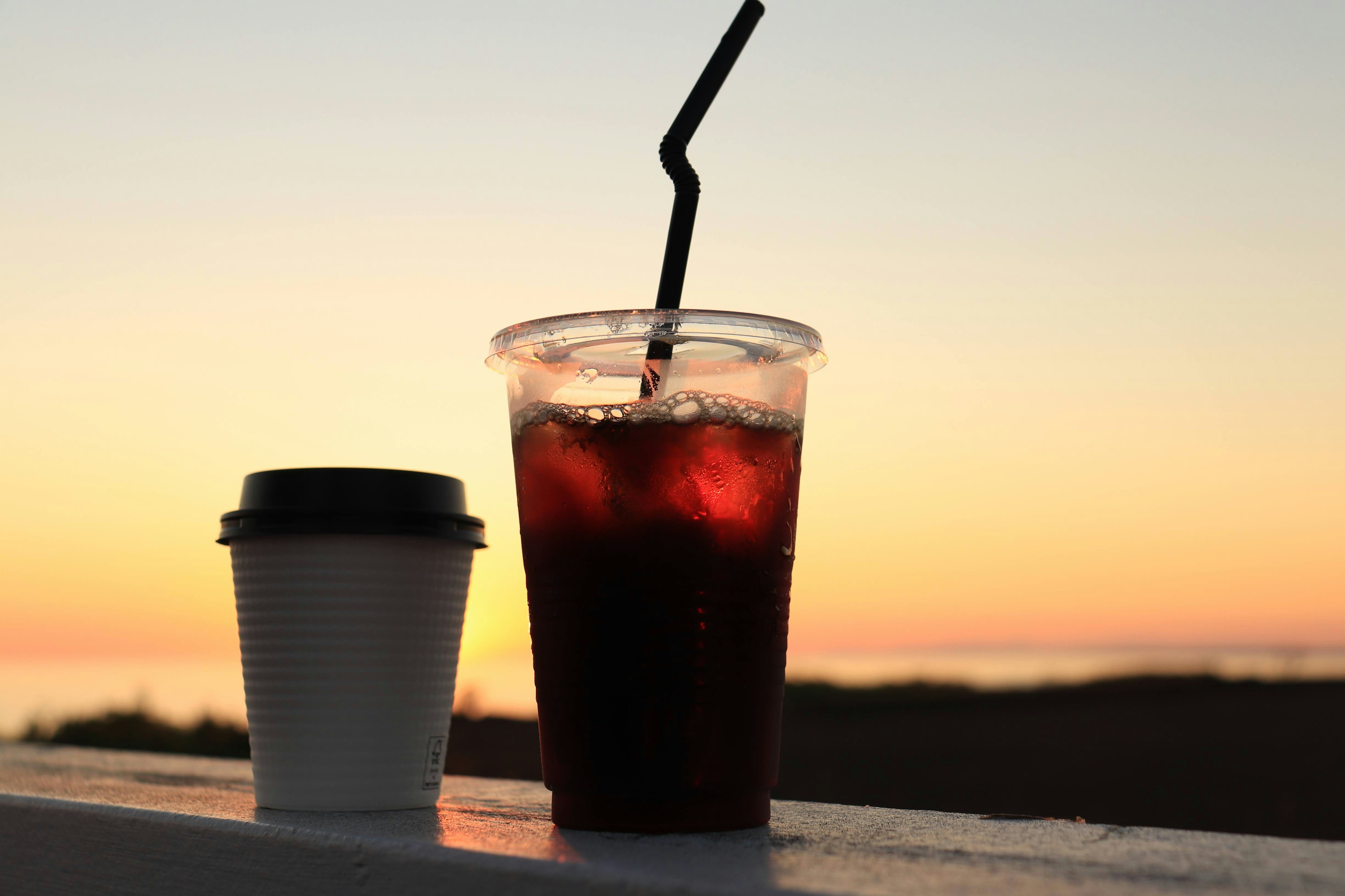 Silhouette of iced drink and coffee cup against sunset