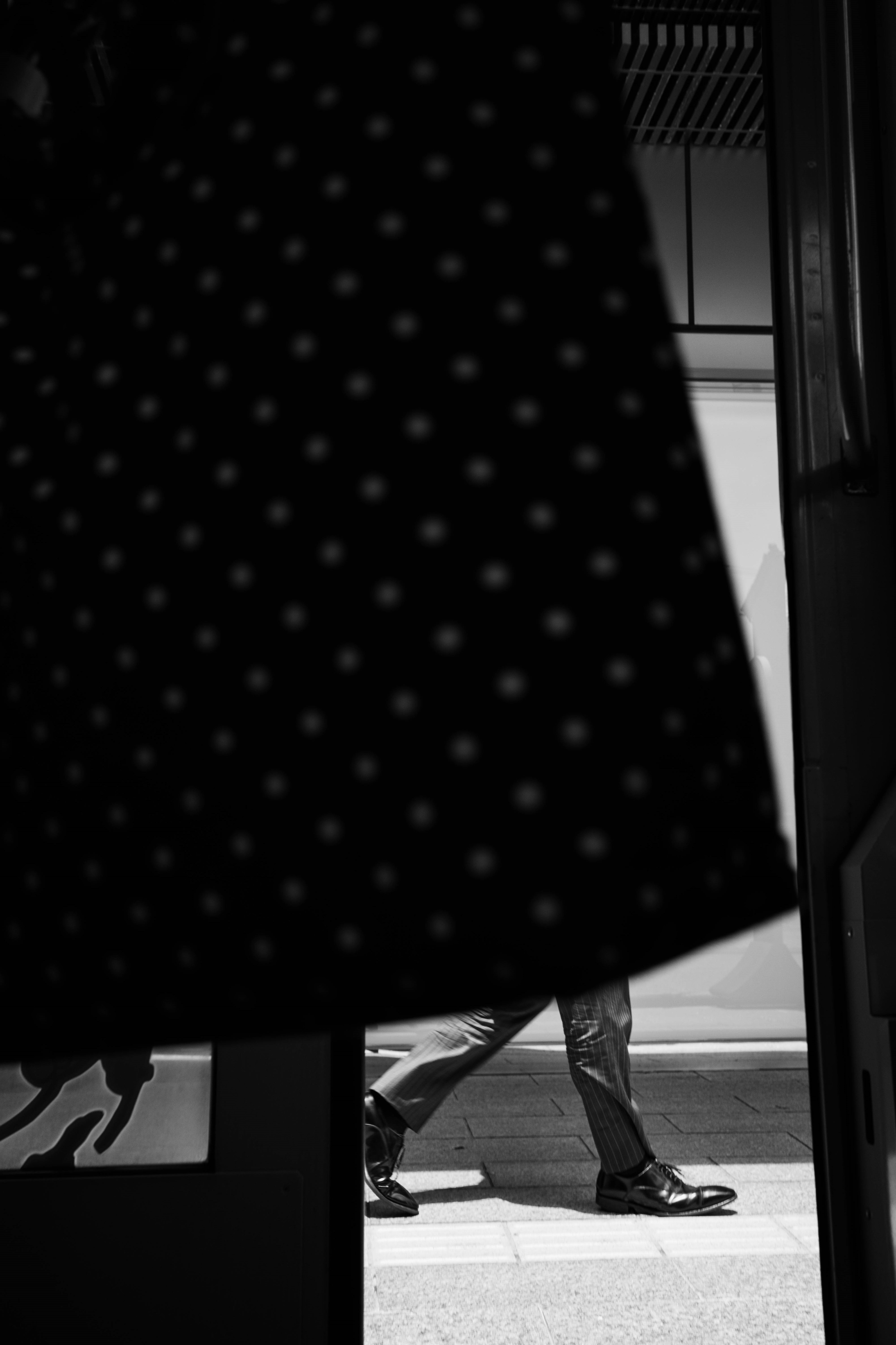 Black and white image showing a person walking behind a polka dot fabric