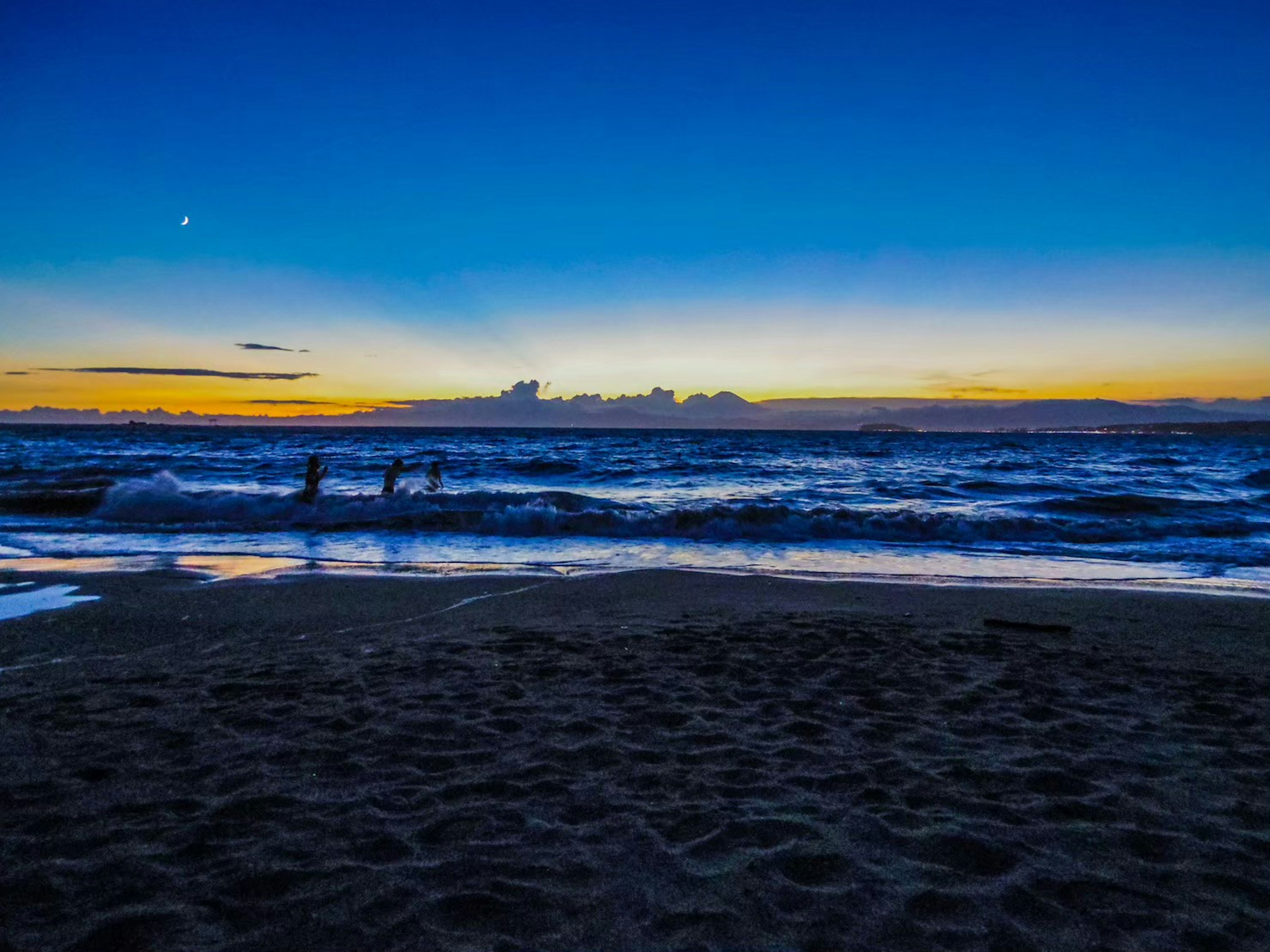 Silhouetted people wading in the waves at sunset beach