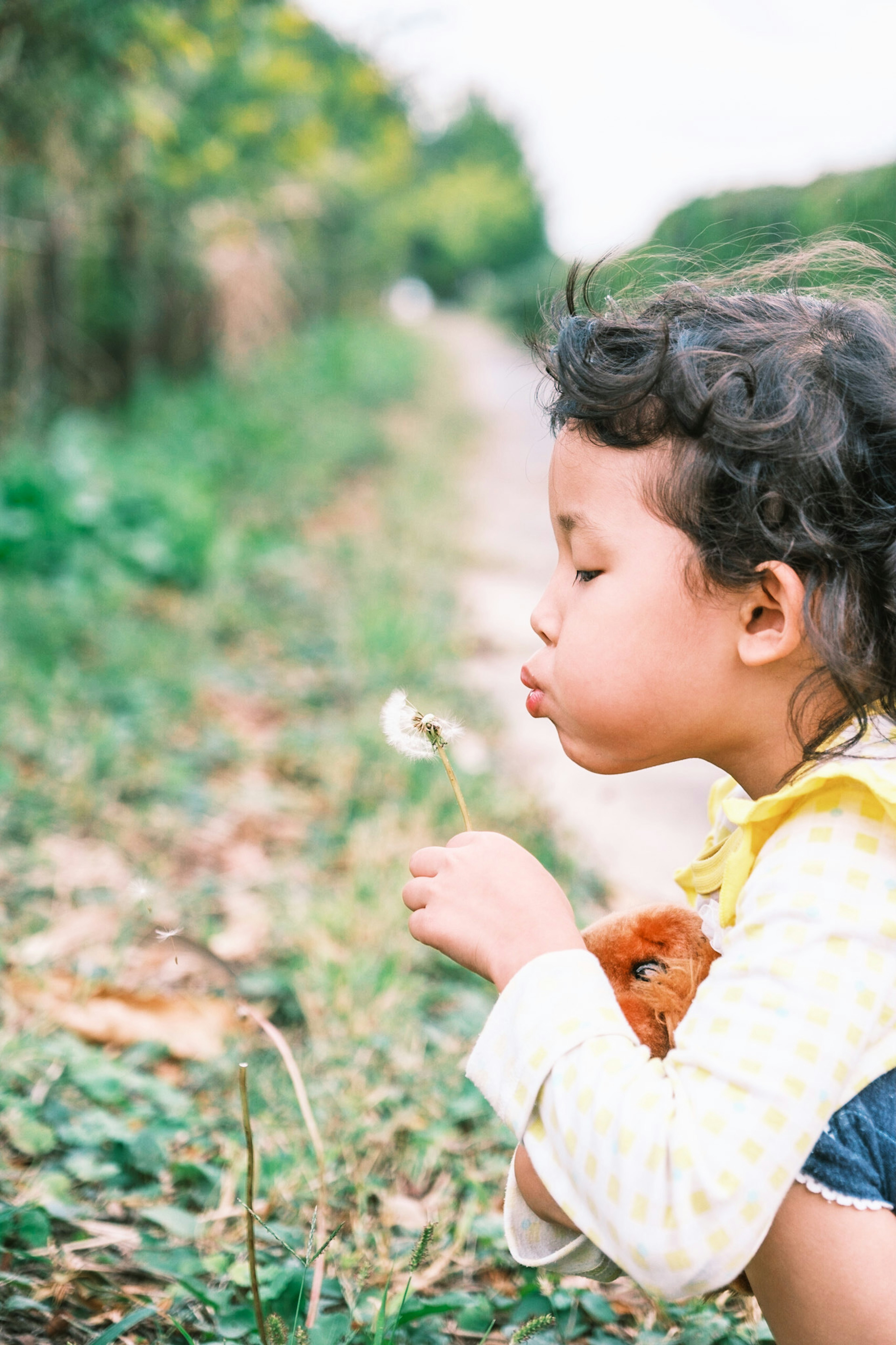 A young girl blowing on a dandelion puff in a grassy area