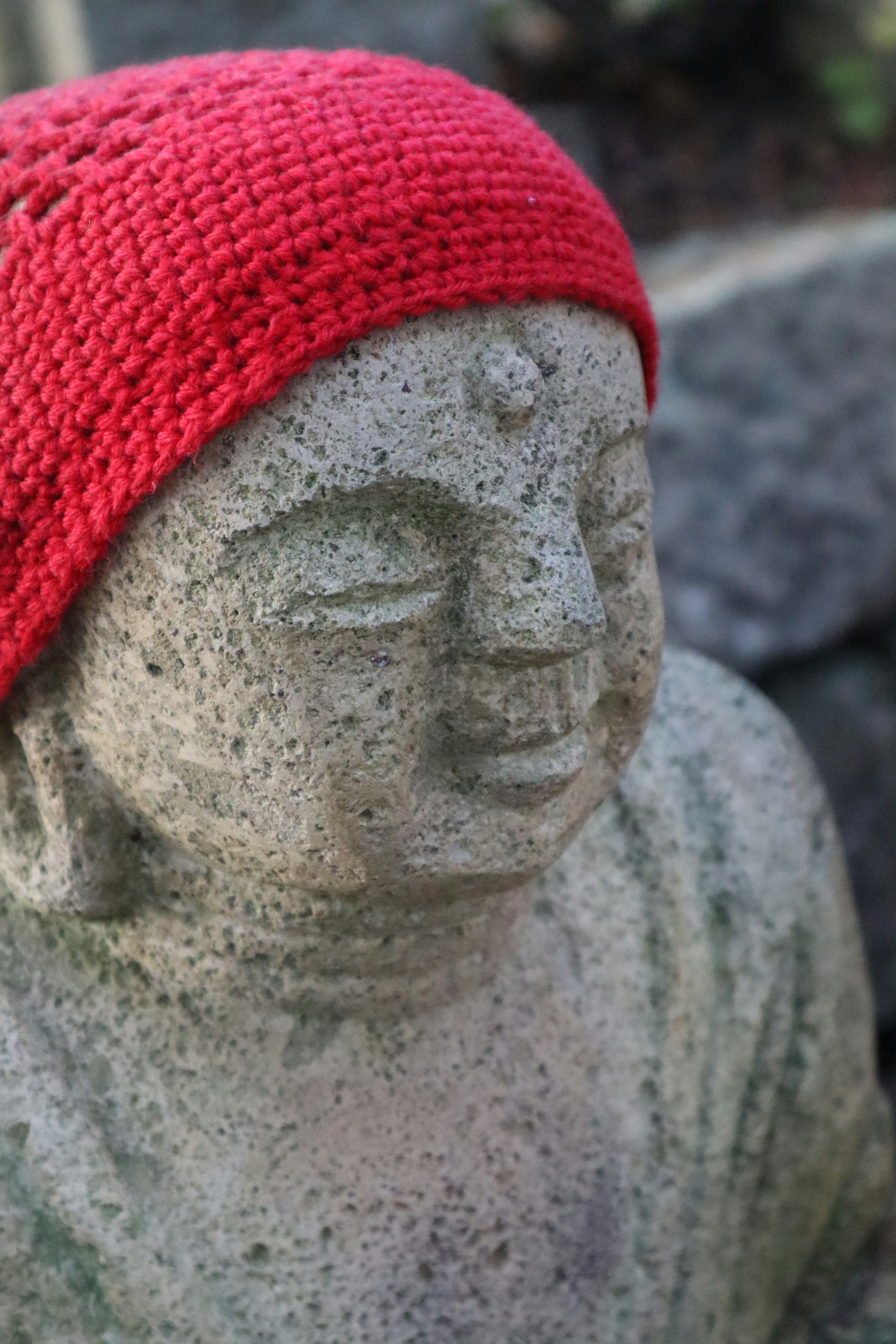 Close-up of a stone Buddha statue wearing a red hat