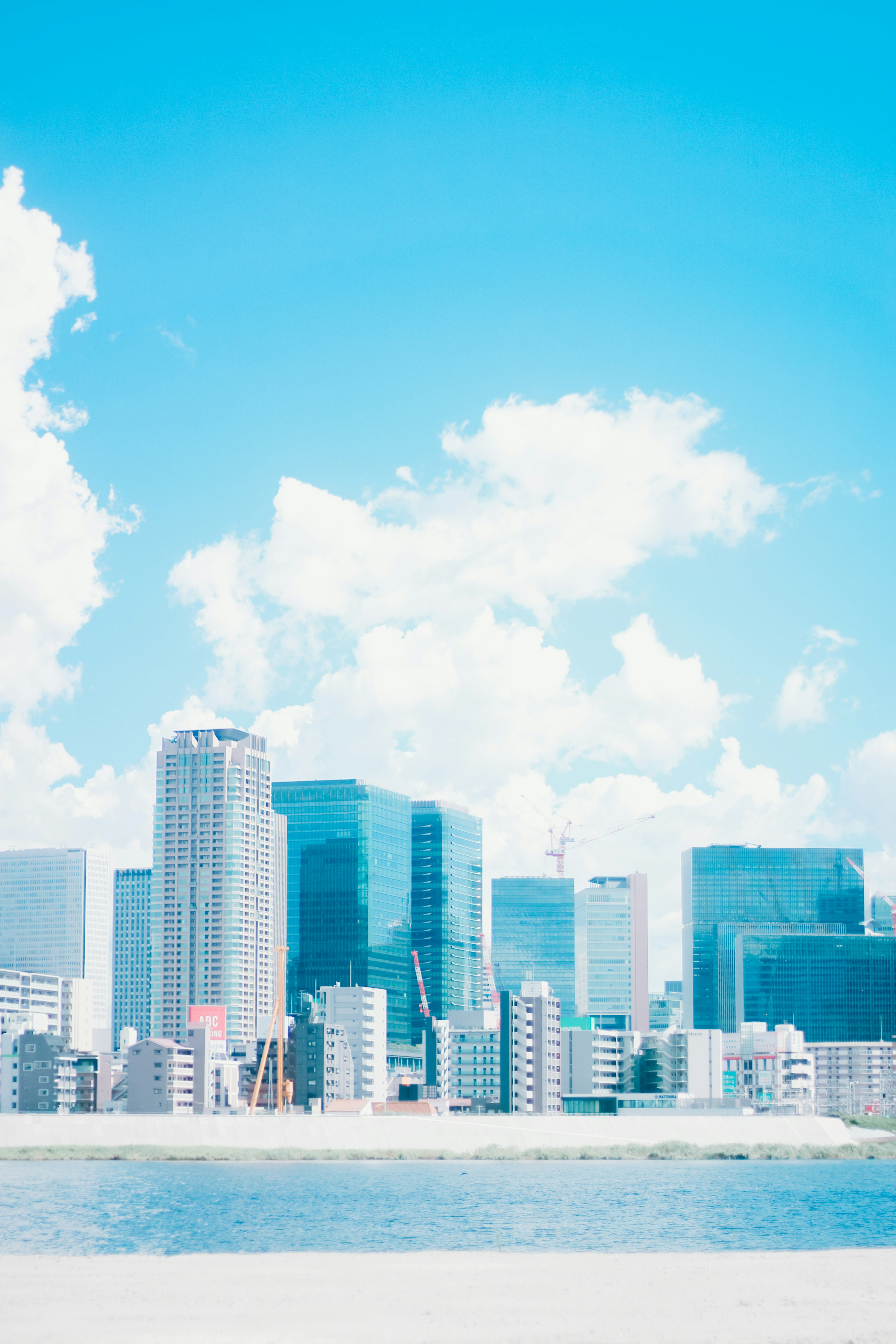 Urban skyline under a bright blue sky with clouds featuring tall buildings and a river