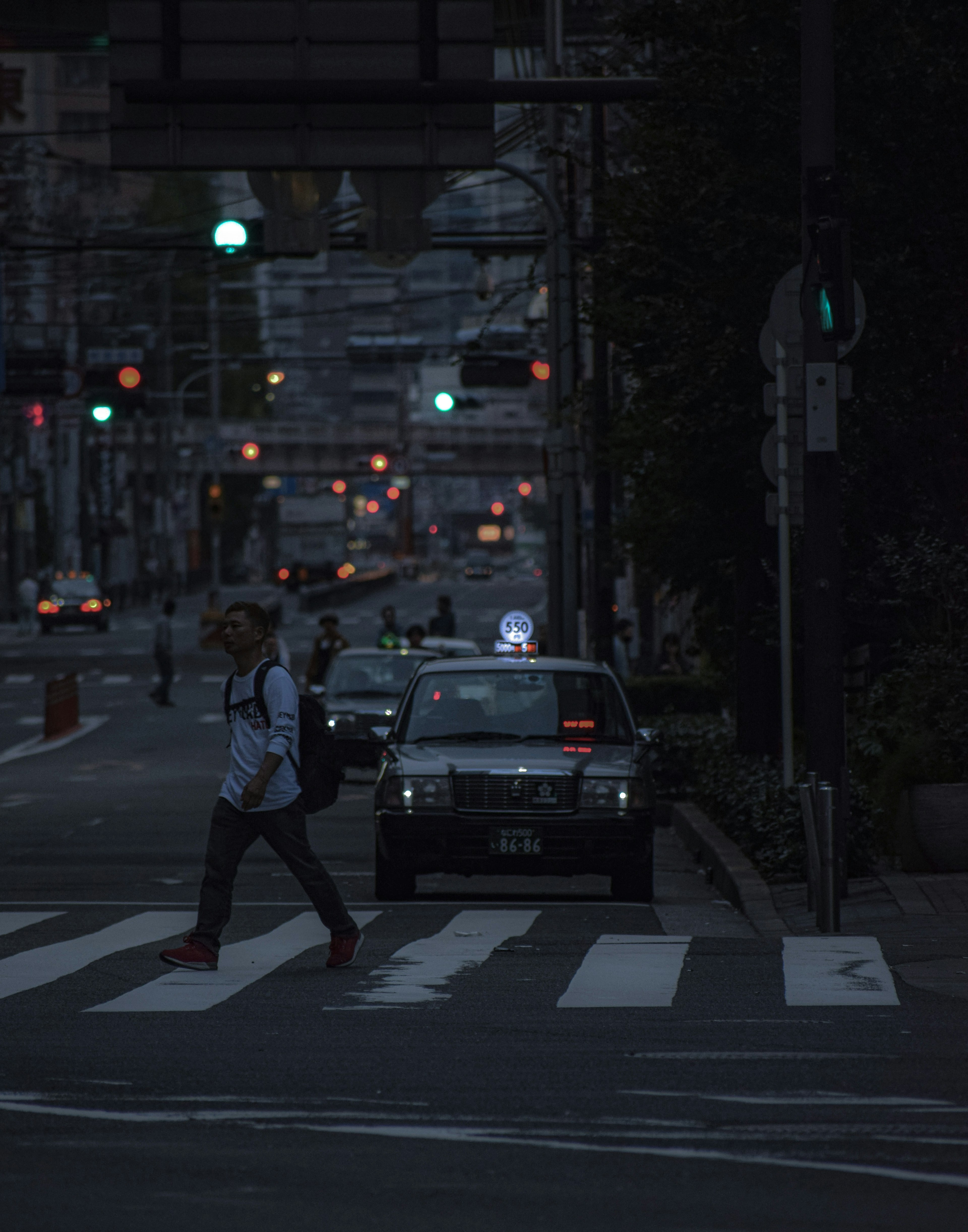 Pedone che attraversa la strada di notte con un taxi sullo sfondo