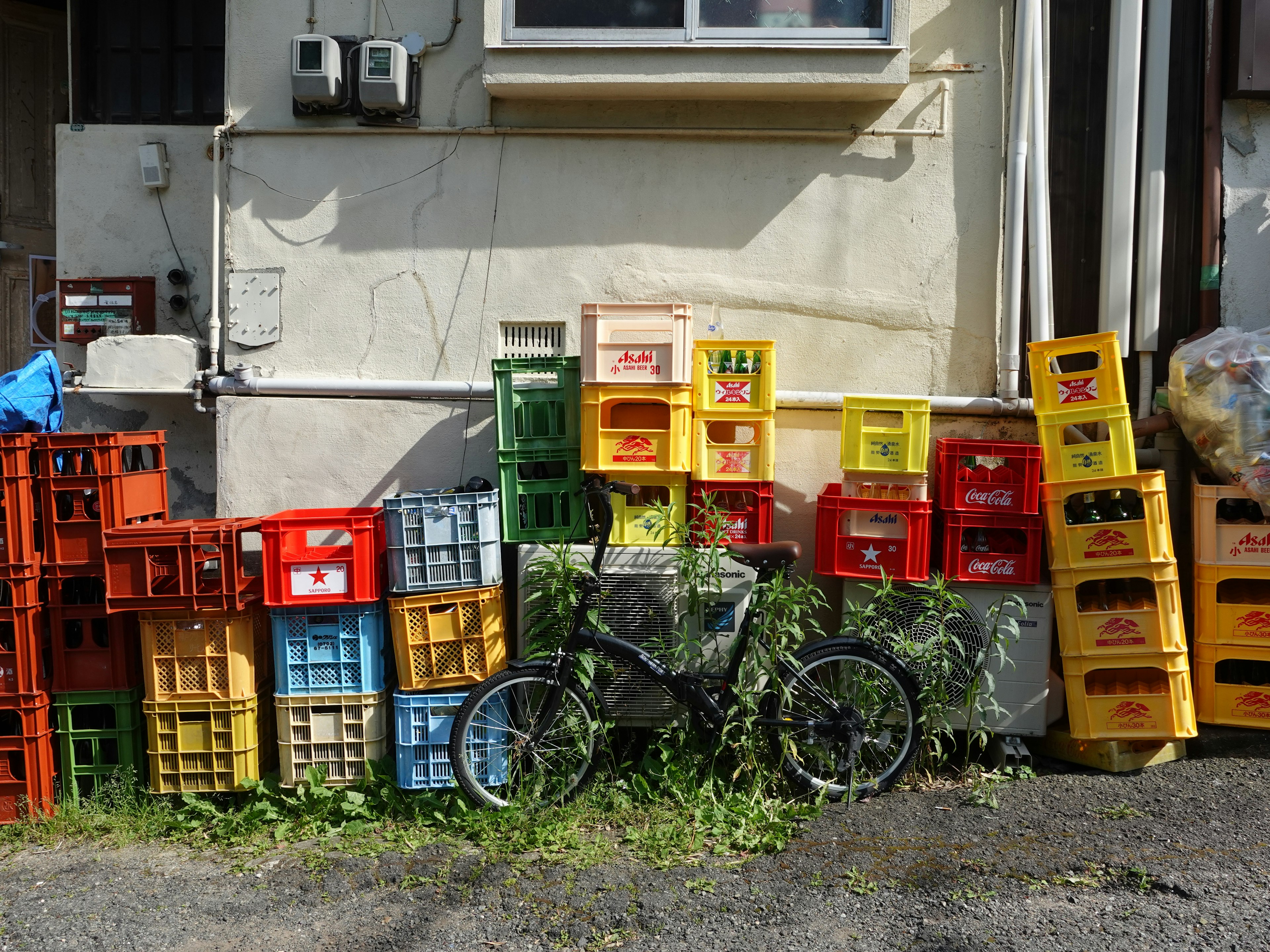 Una escena con cajas vacías de colores apiladas contra una pared con una bicicleta al lado