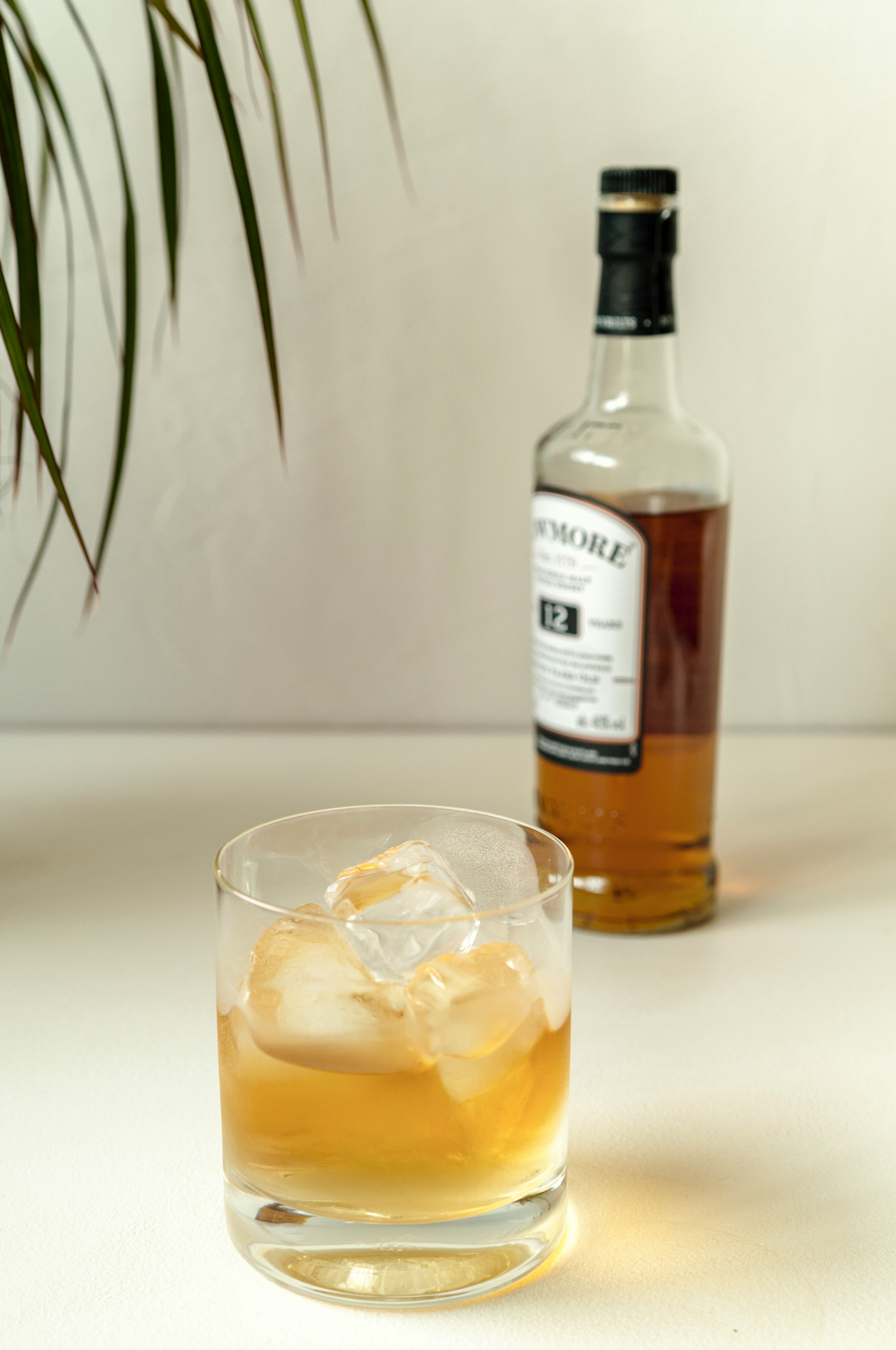 Vaso de whisky con hielo y una botella sobre una mesa simple