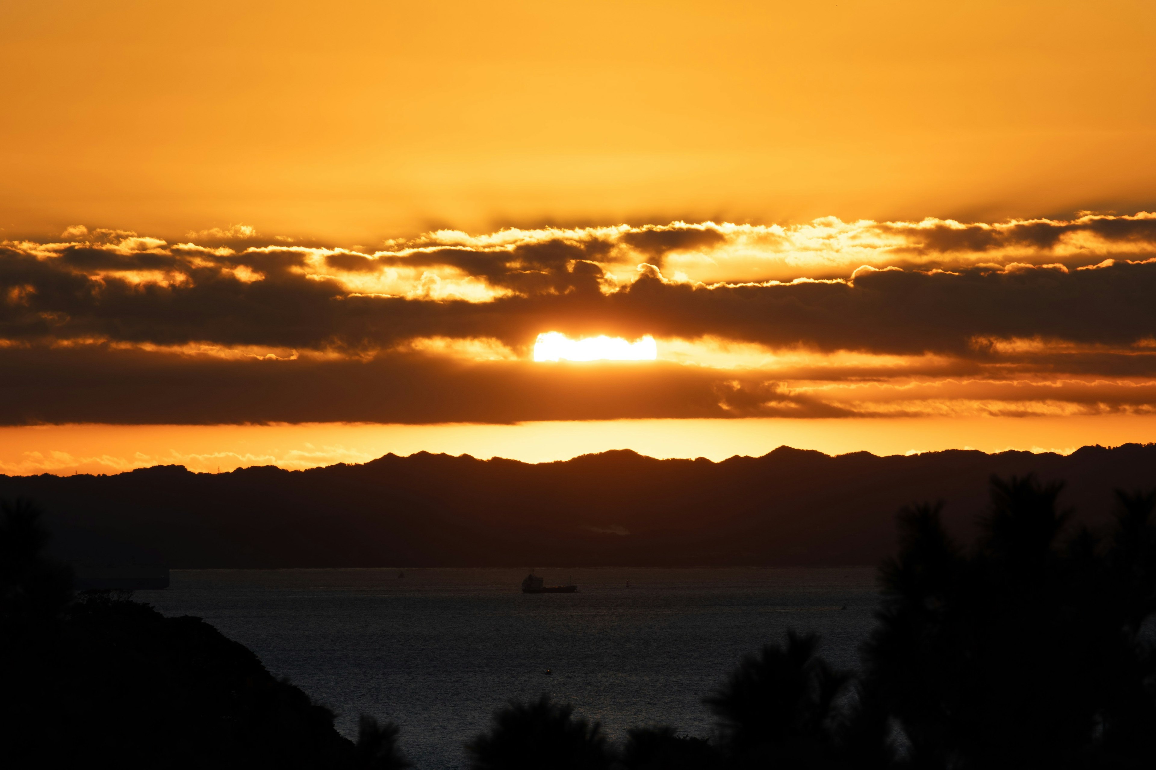 夕日が海に沈む美しい風景 黒いシルエットの山々とオレンジ色の空