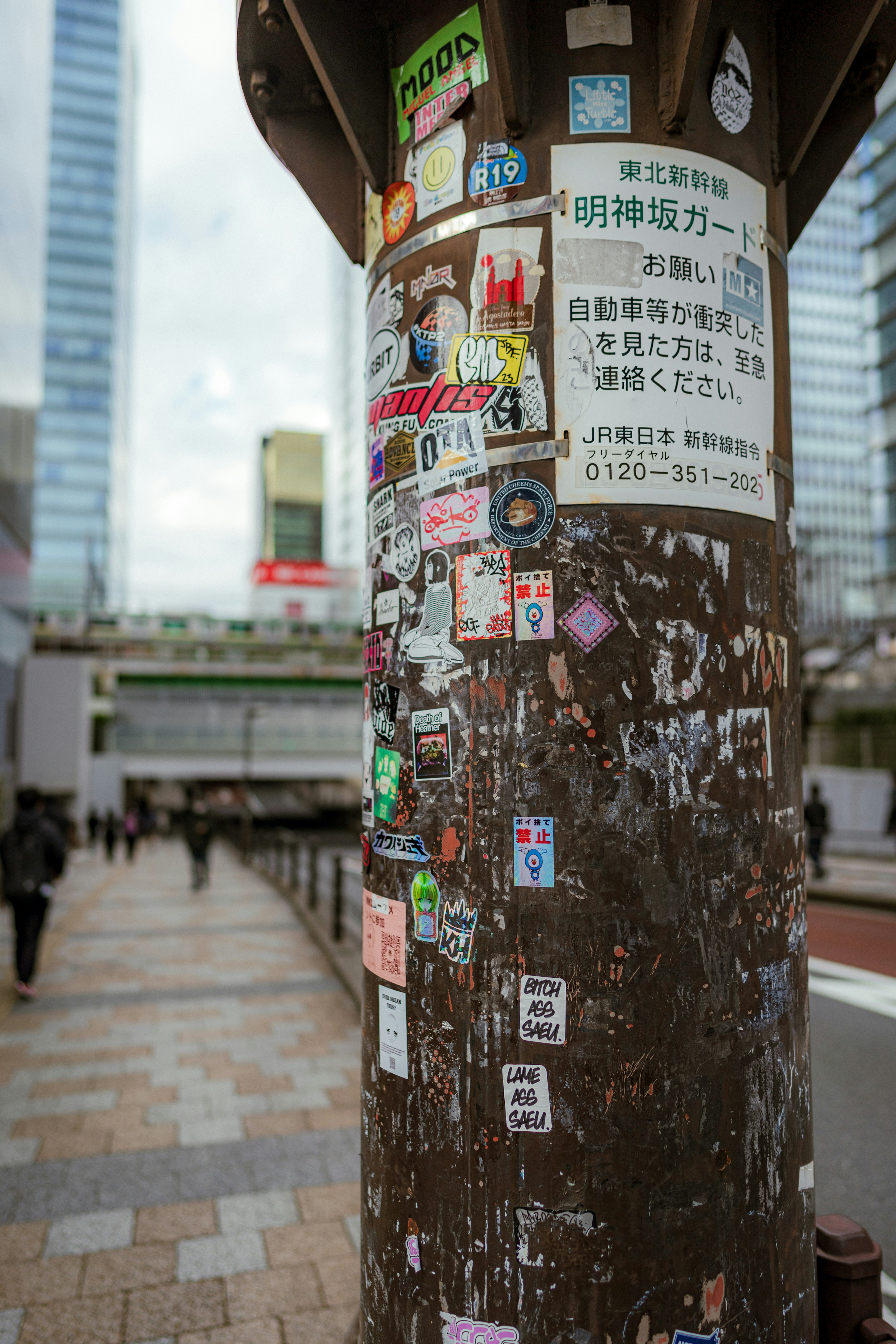 多くのステッカーが貼られた柱と周囲のビル群