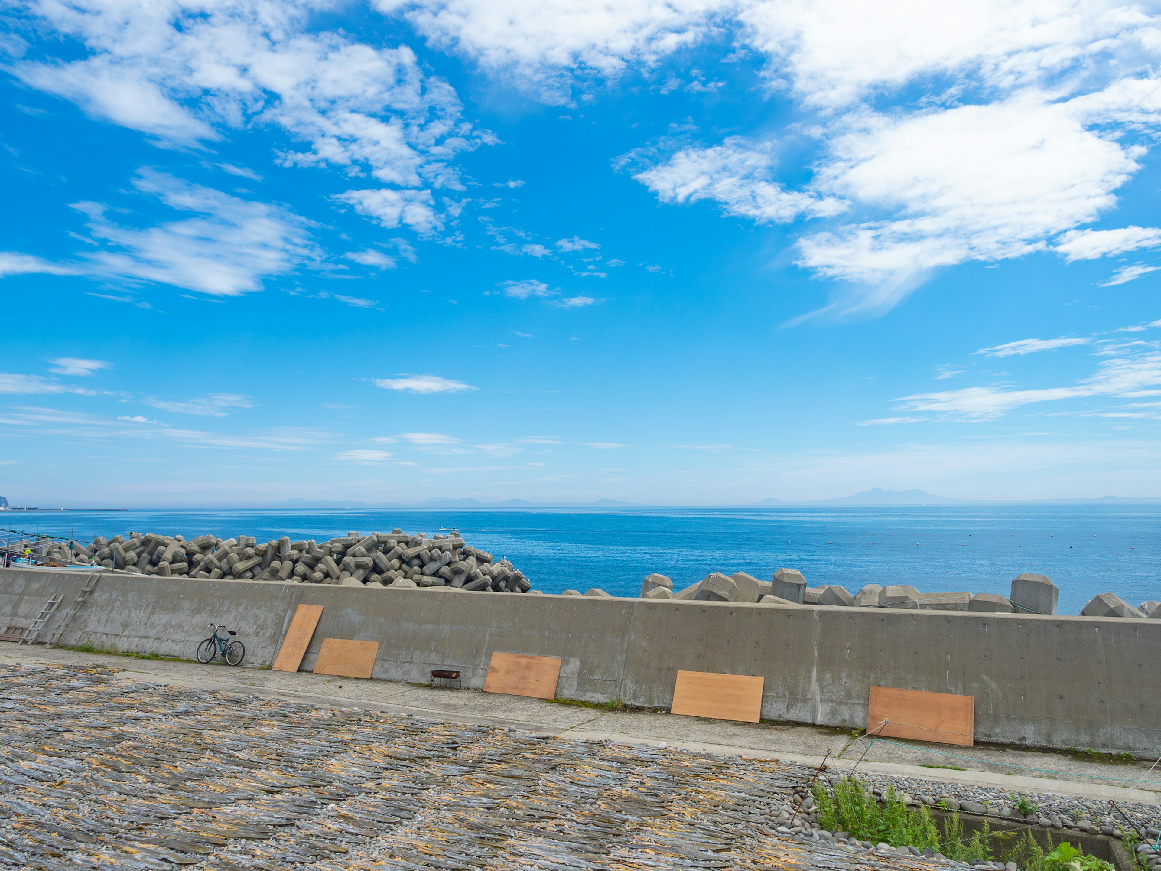 Stone breakwater and paved path with bright blue sky and ocean view