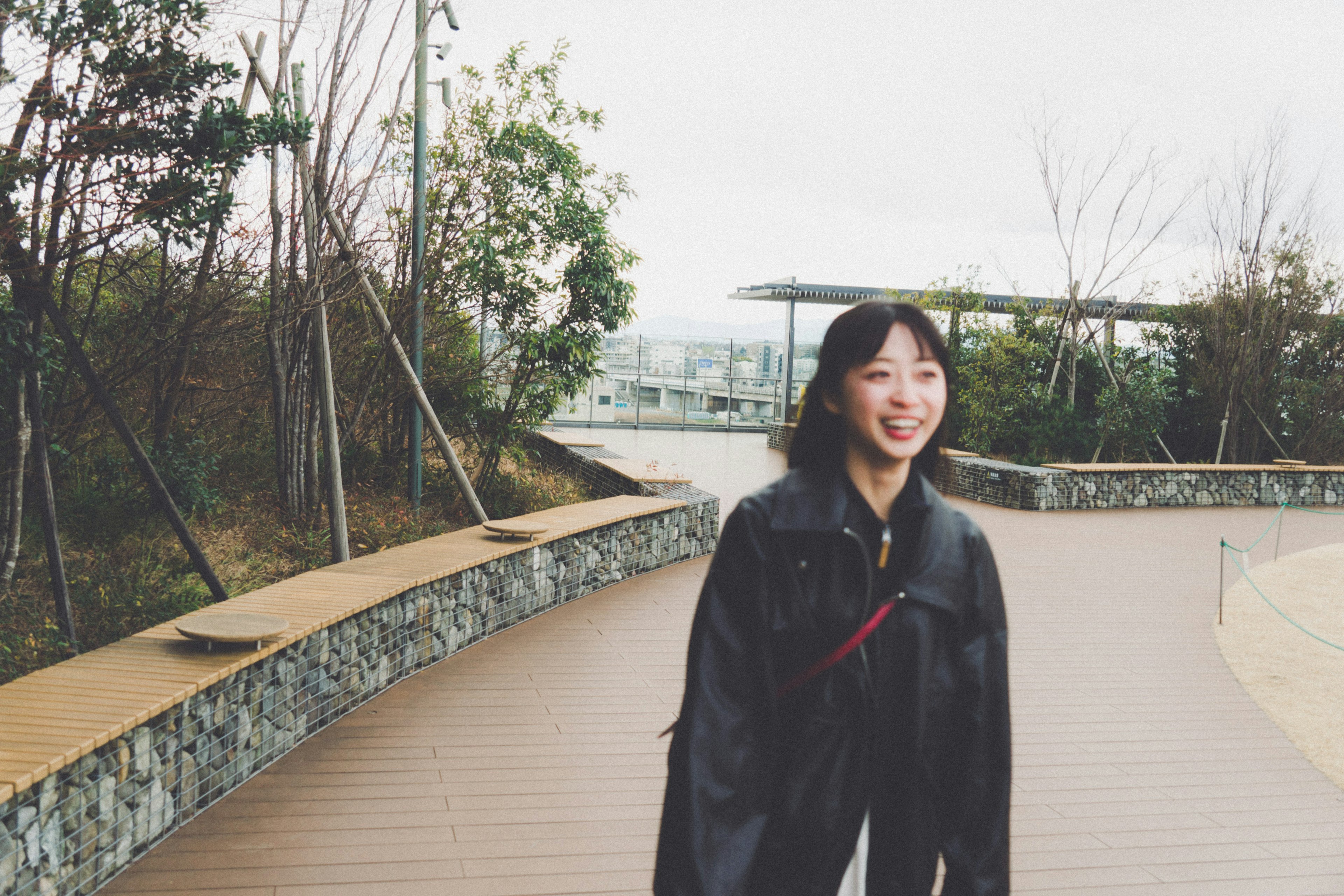 公園の小道を歩く女性の笑顔の写真 緑の植物と木々が背景にある