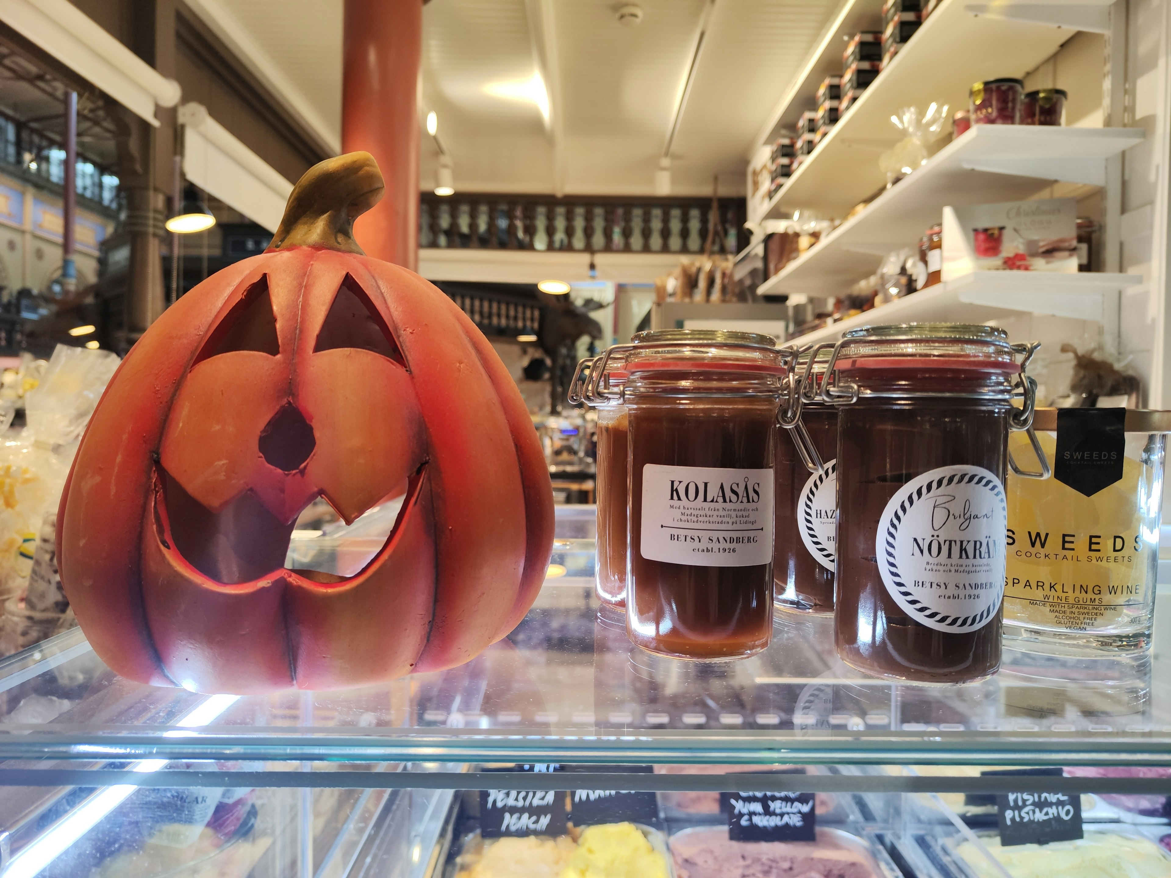 Halloween pumpkin with carved face next to jars of jam in a store display