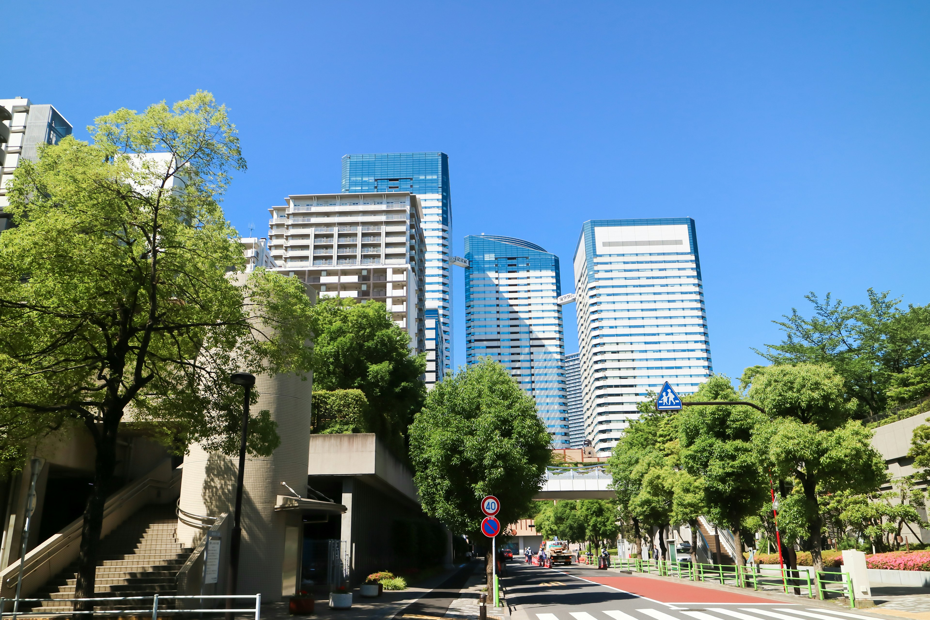 Cityscape with skyscrapers under clear blue sky green trees and sidewalk visible