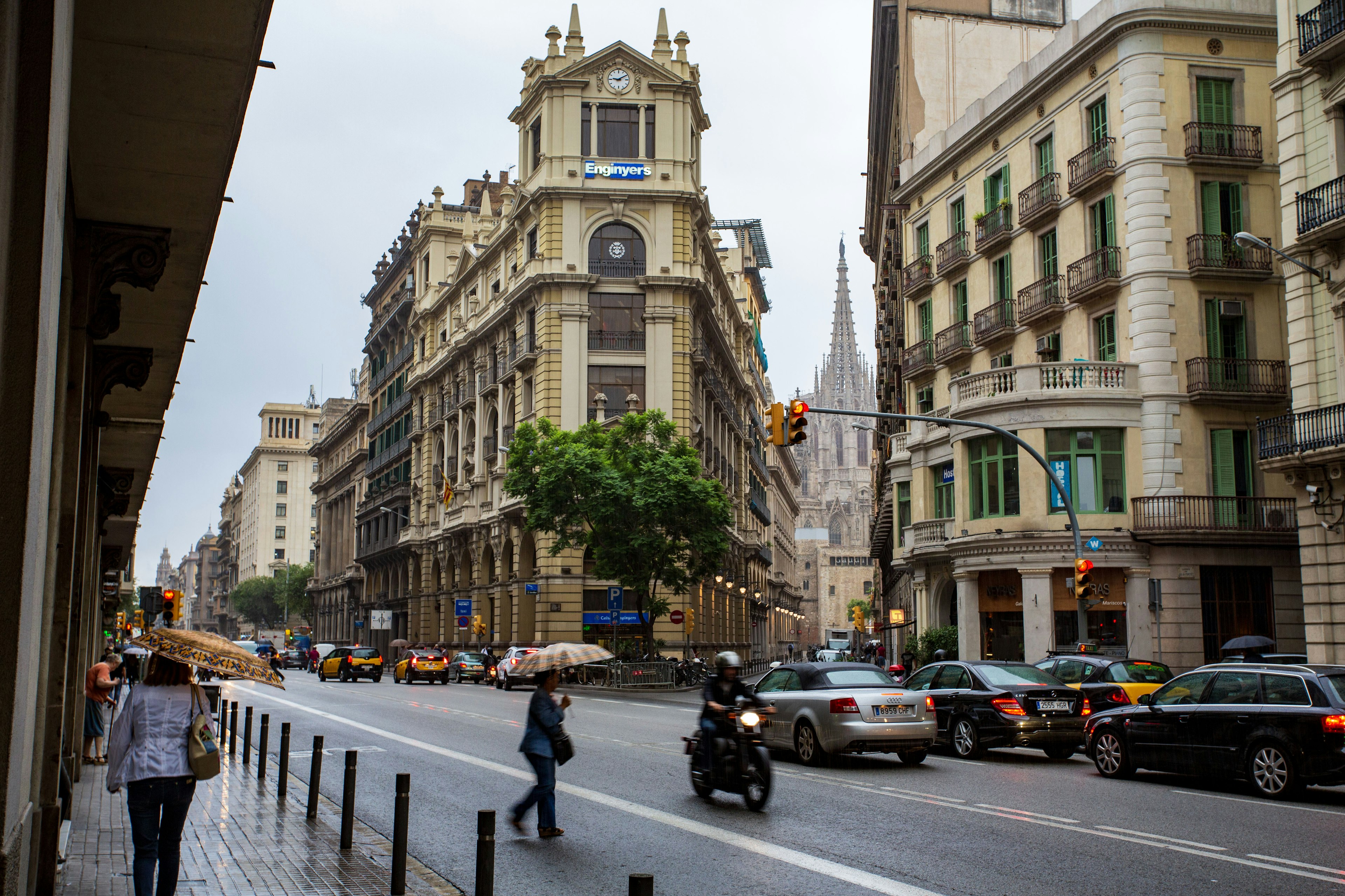 Escena callejera de Barcelona con peatones y motocicletas bajo la lluvia