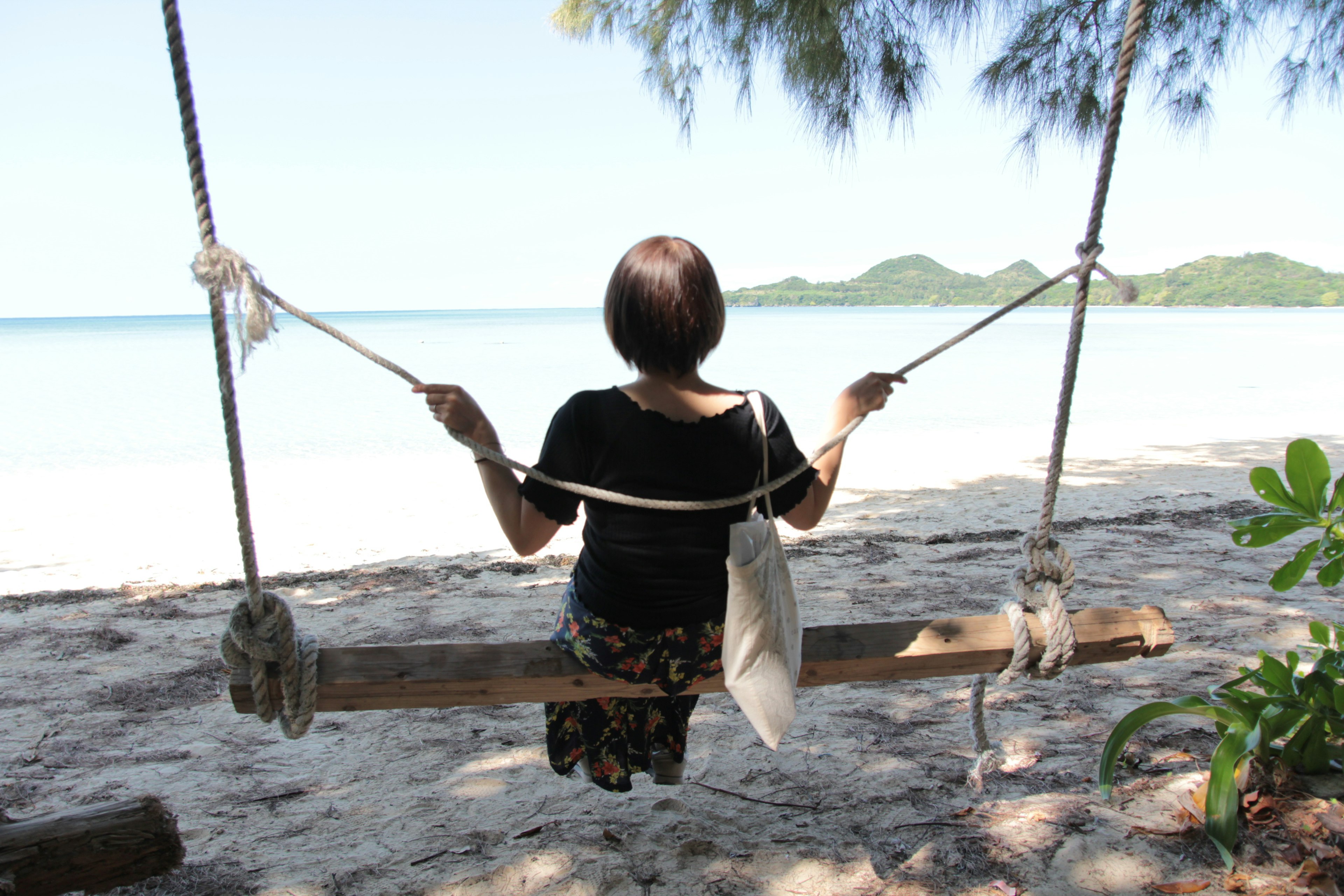 ビーチでブランコに座る女性の後ろ姿と青い海の風景