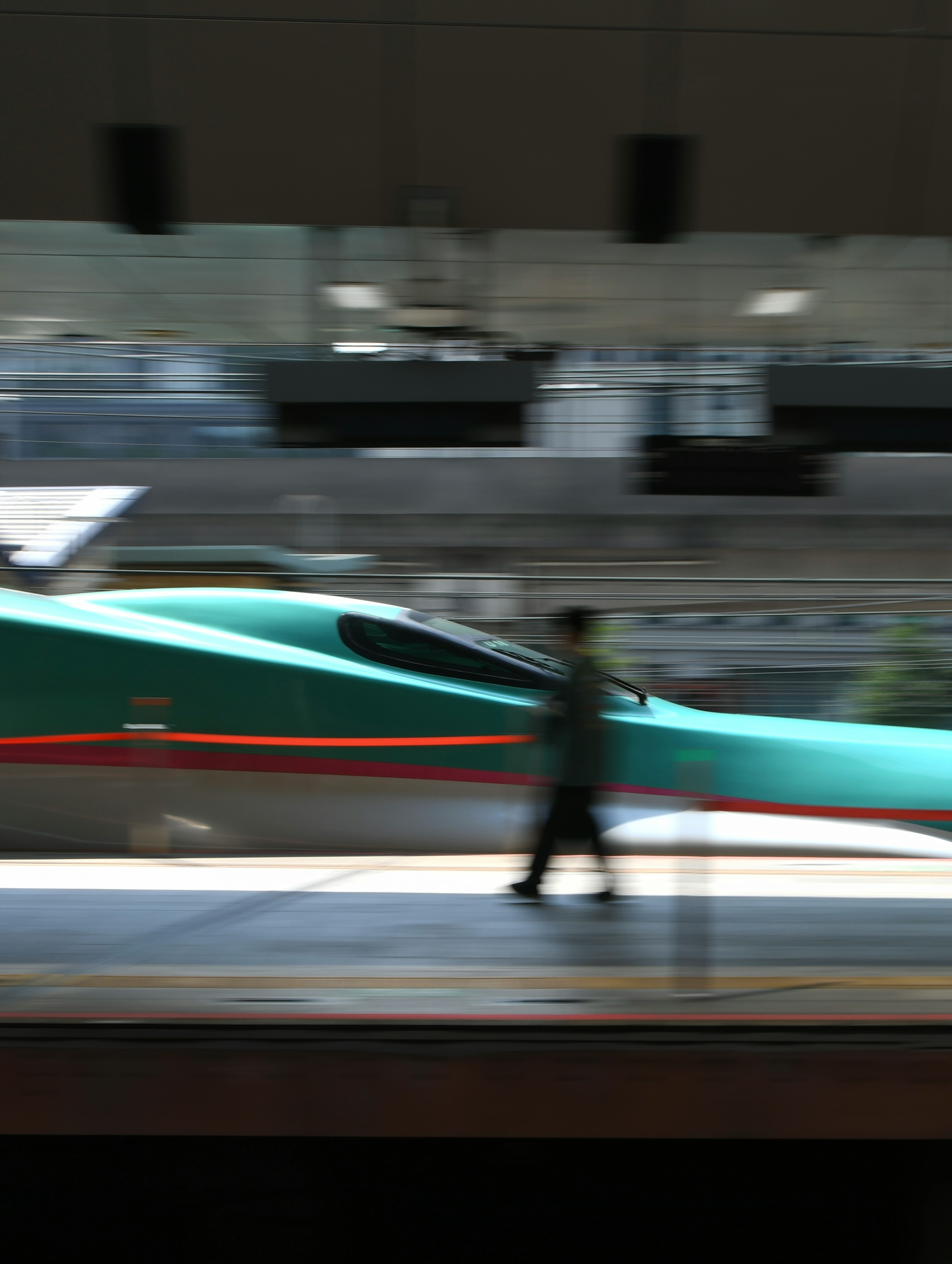 流れるようなデザインの新幹線が駅に停車している様子とその前を歩く人