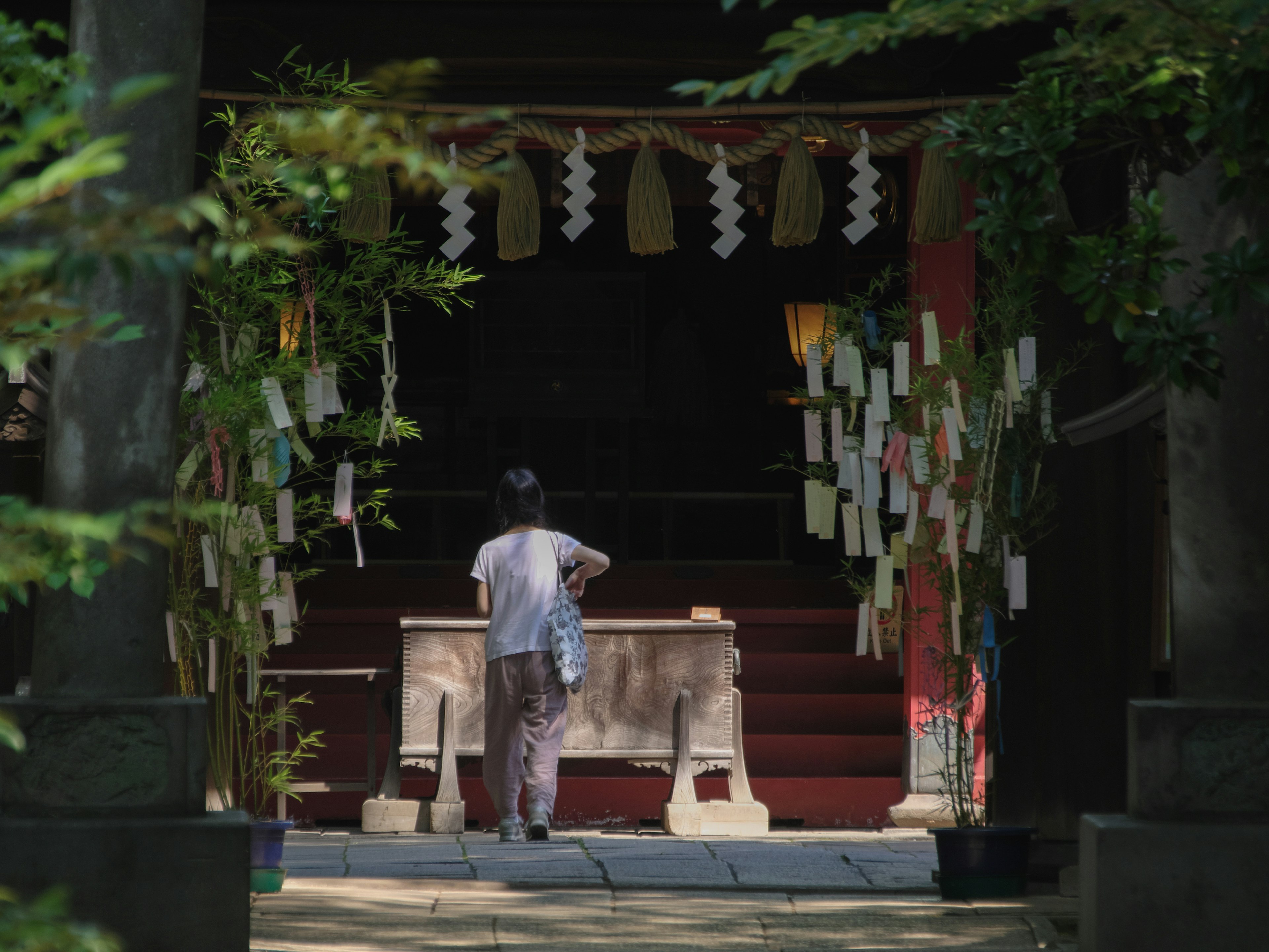 A person praying at the entrance of a shrine surrounded by greenery