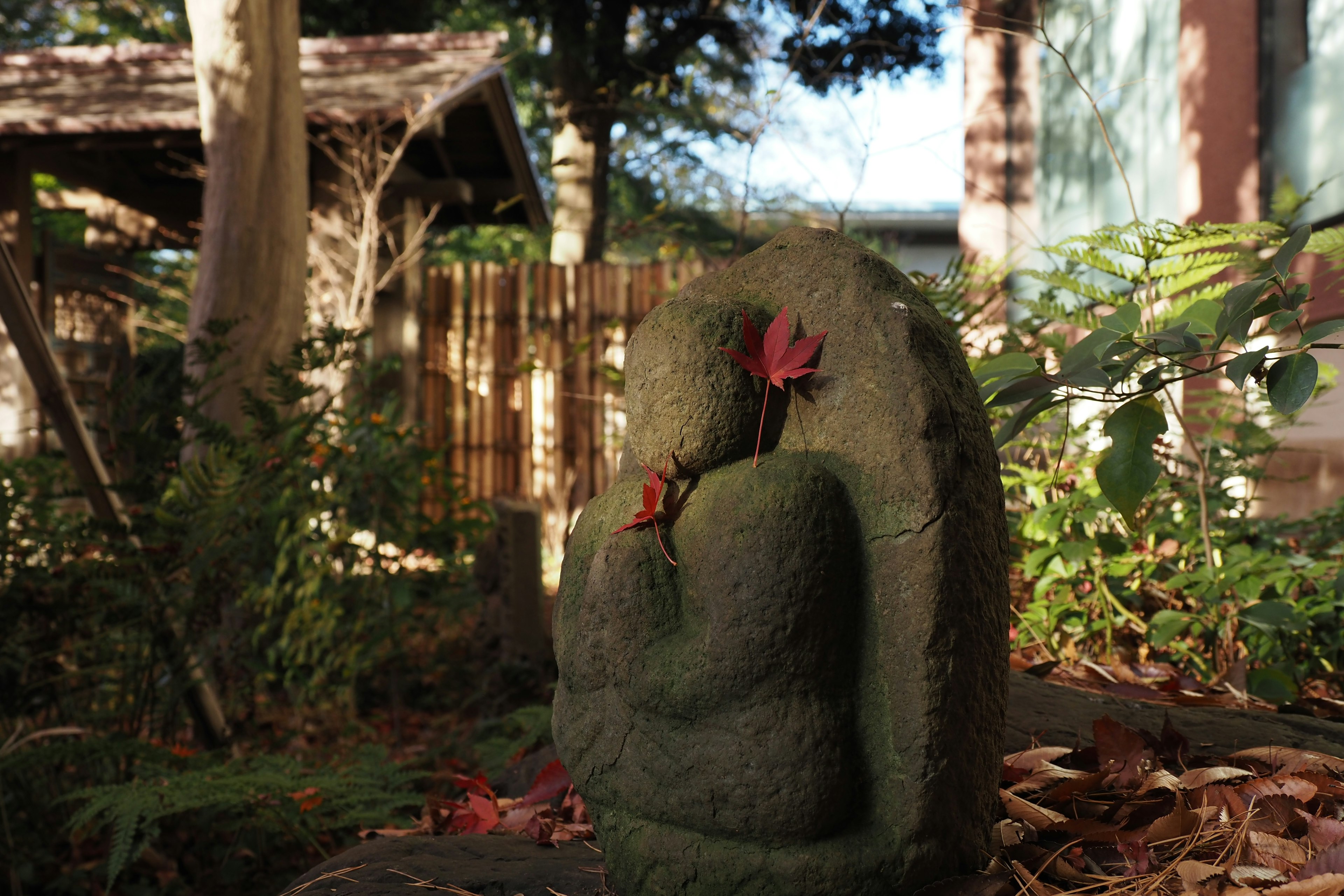 A moss-covered stone statue of a Buddha with autumn leaves in a serene garden