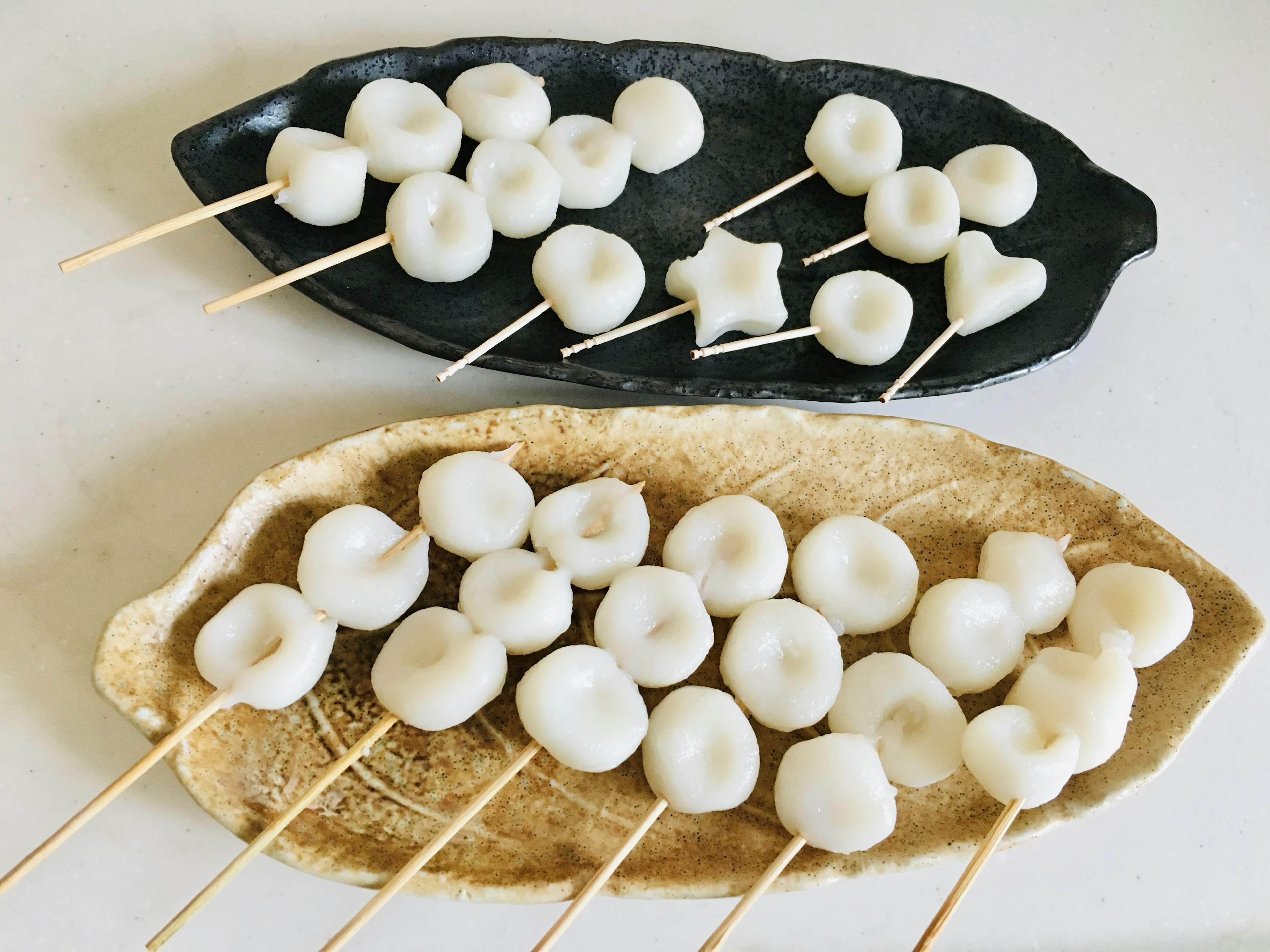 Dua piring dengan dumpling putih di tusuk sate disusun dalam berbagai bentuk