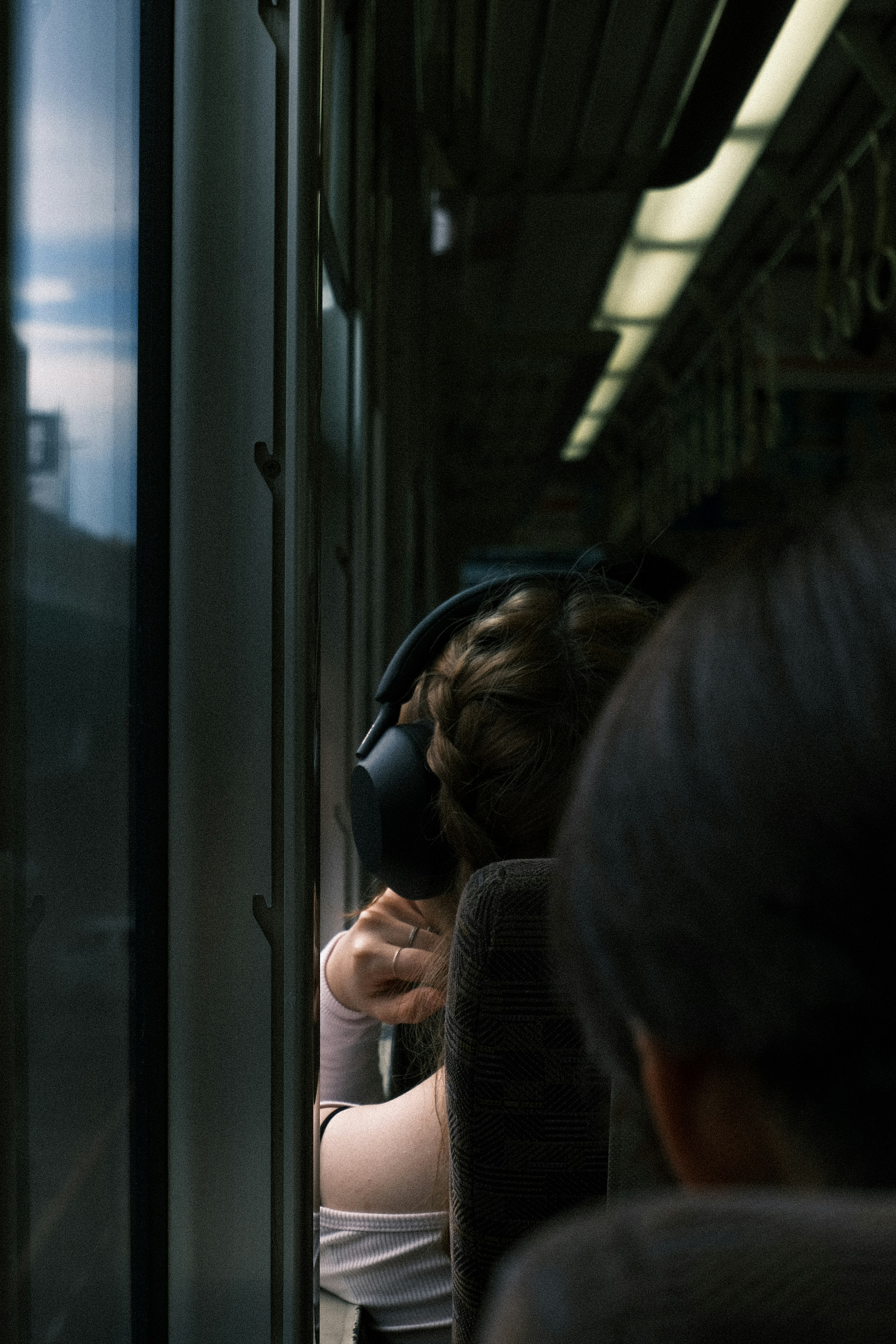 Una mujer relajándose junto a la ventana del tren con auriculares y un pasajero sentado detrás